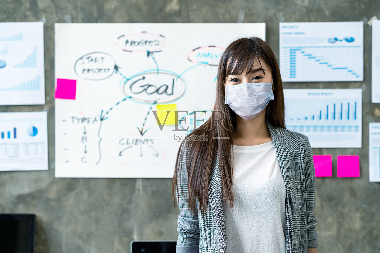 年轻的亚洲女性工人戴着医用口罩防护看着镜头，戴着外科口罩在办公室工作空间微笑，在概念上回到工作岗位，重新开业，预防冠状病毒。照片摄影图片
