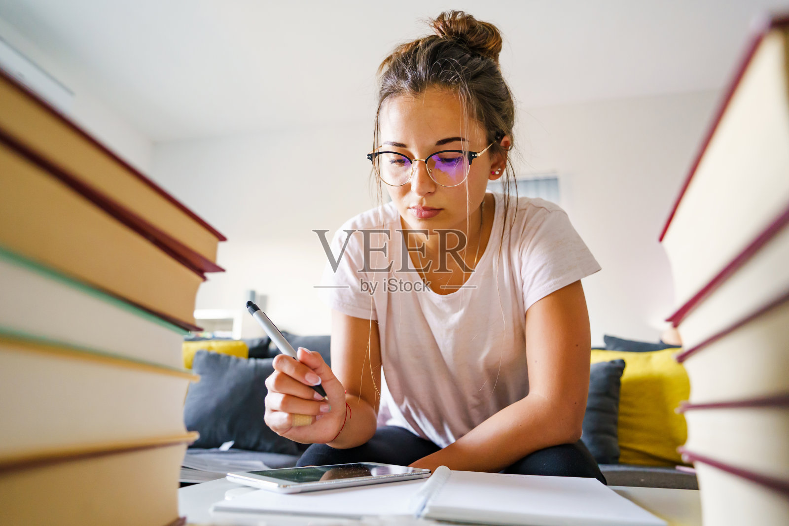 年轻的白人女学生坐在家里的桌子旁，用成堆的书阅读和写作，同时研究考试教育和学习的概念照片摄影图片