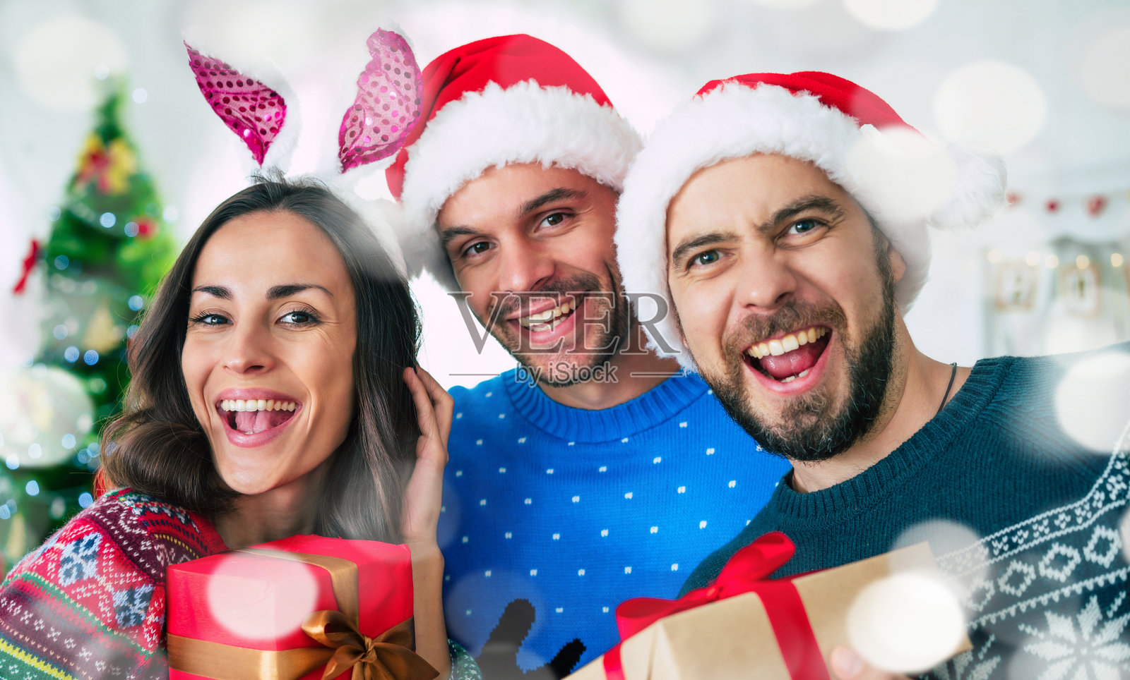 一群兴奋的美丽的朋友在圣诞老人的帽子有乐趣，而派对在家里的圣诞树背景照片摄影图片