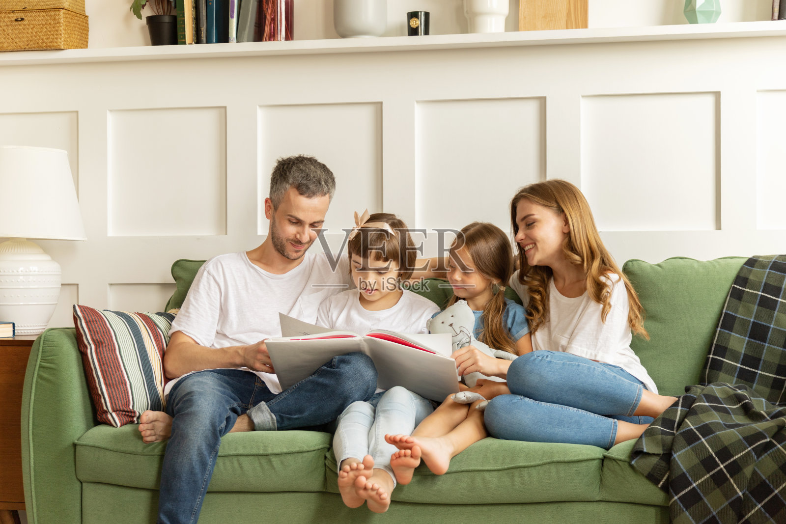 爱年轻的家庭和小女儿在舒适的客厅里读书，快乐的为人父母照片摄影图片