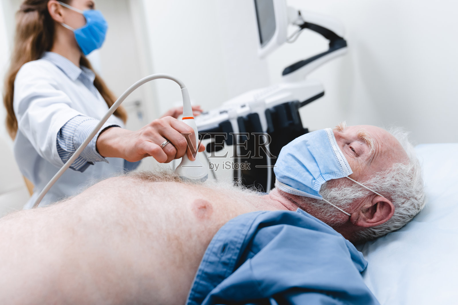 一名年长病人戴上口罩，由戴口罩的女医生进行超声波胸部检查照片摄影图片