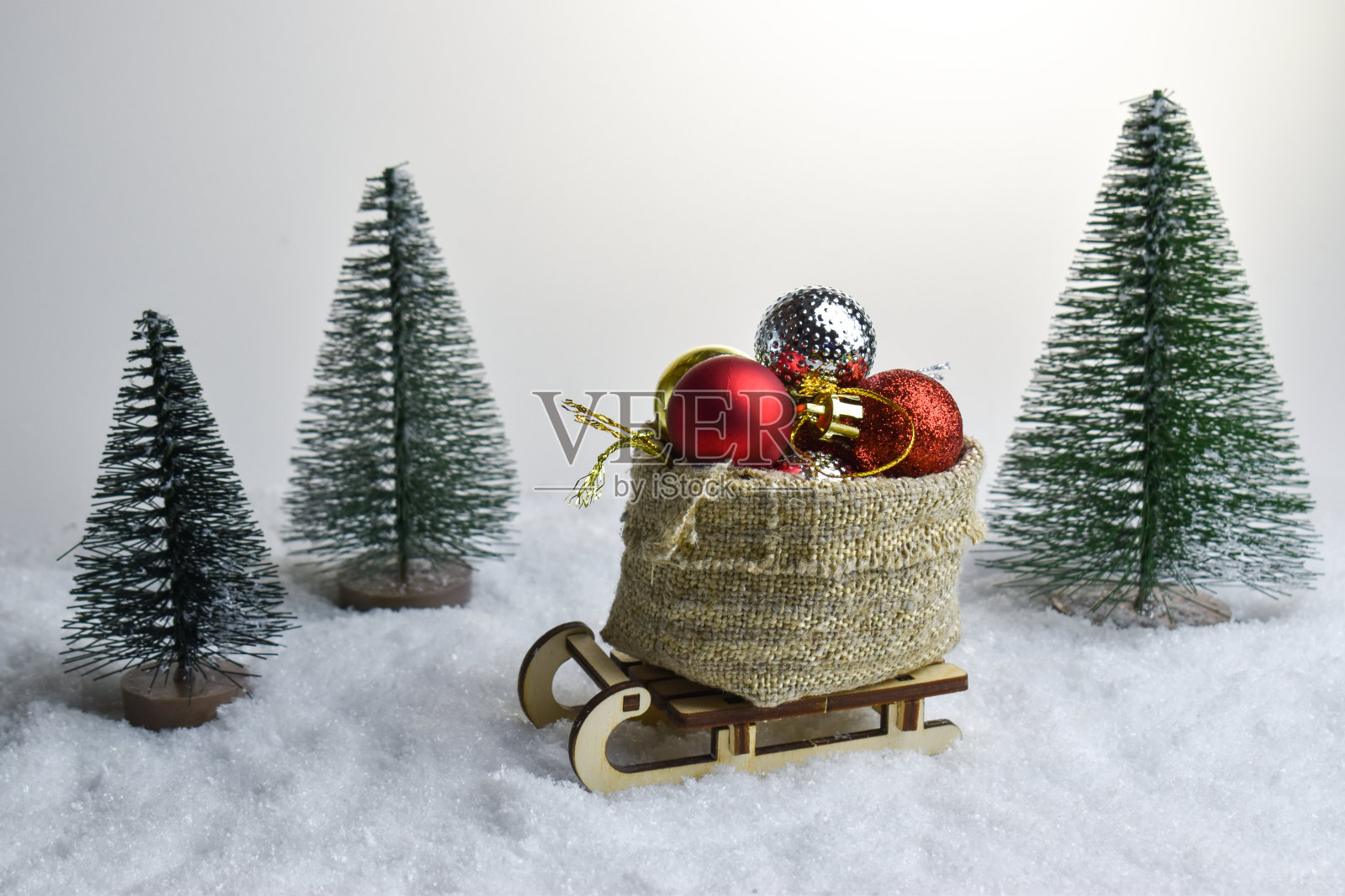 木制雪橇上放着一袋圣诞玩具，背景是雪和圣诞树。新年快乐，圣诞快乐。照片摄影图片