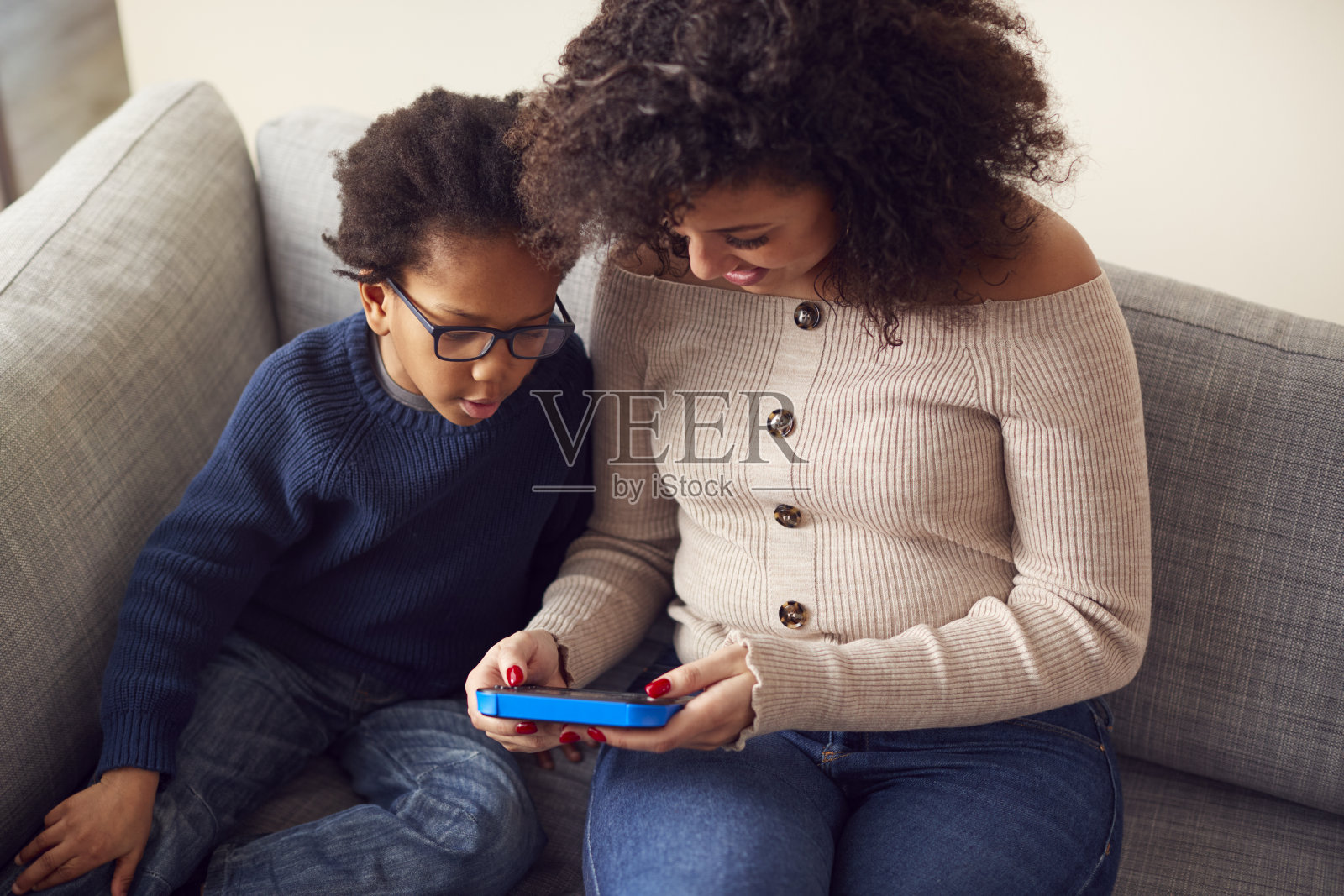 母亲和儿子坐在家里的沙发上一起用手持设备玩电脑游戏照片摄影图片