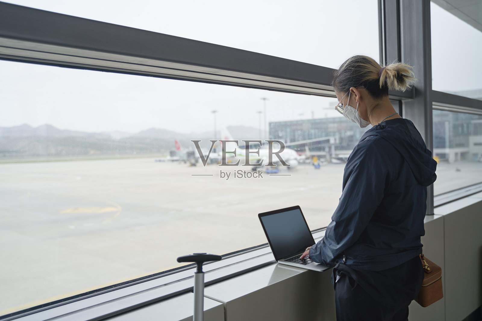 一名亚洲女性乘客在机场等待登机时站在窗口使用笔记本电脑照片摄影图片
