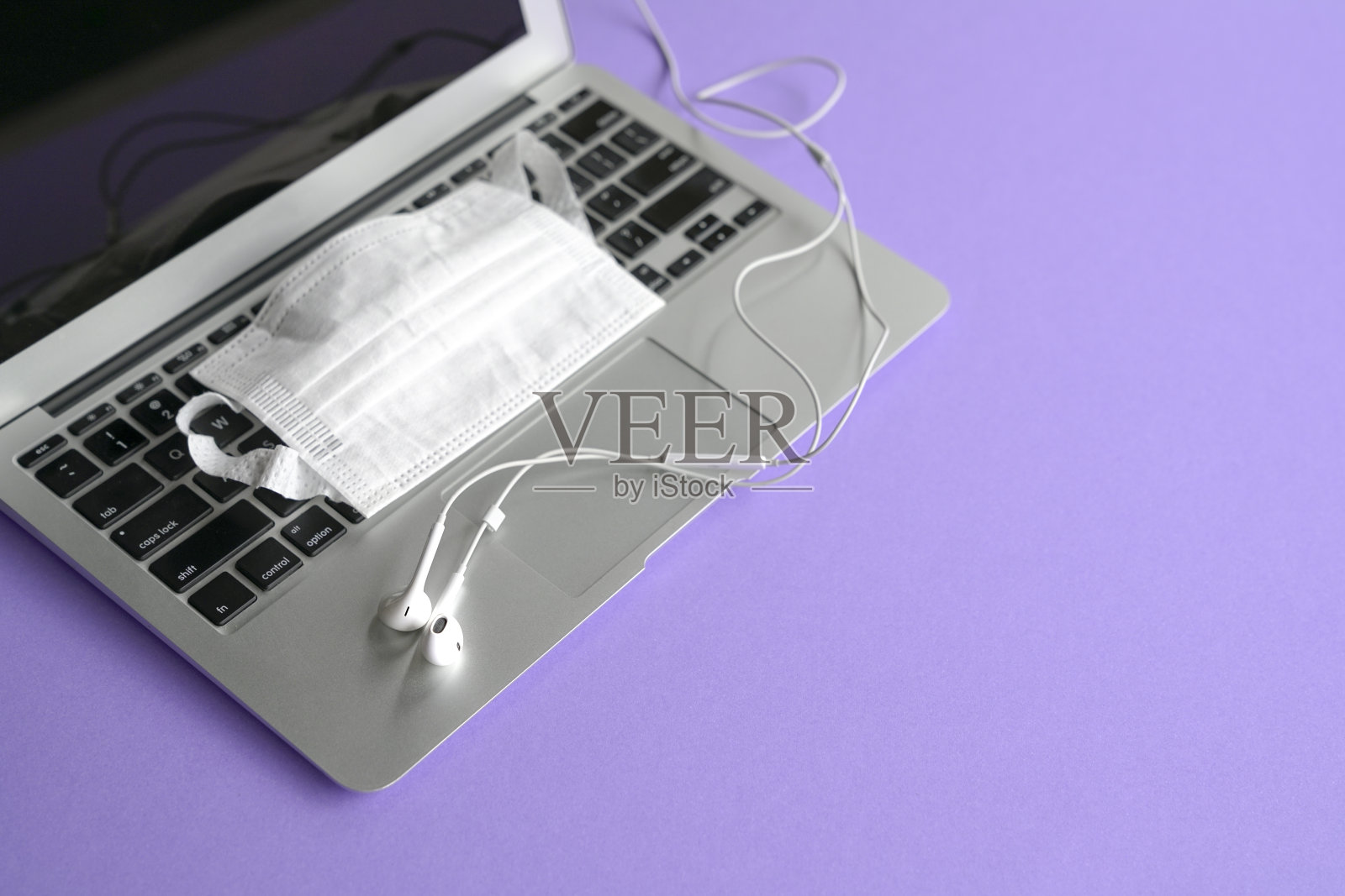 电脑和笔记本电脑上的耳机和面罩。紫色的桌面。照片摄影图片