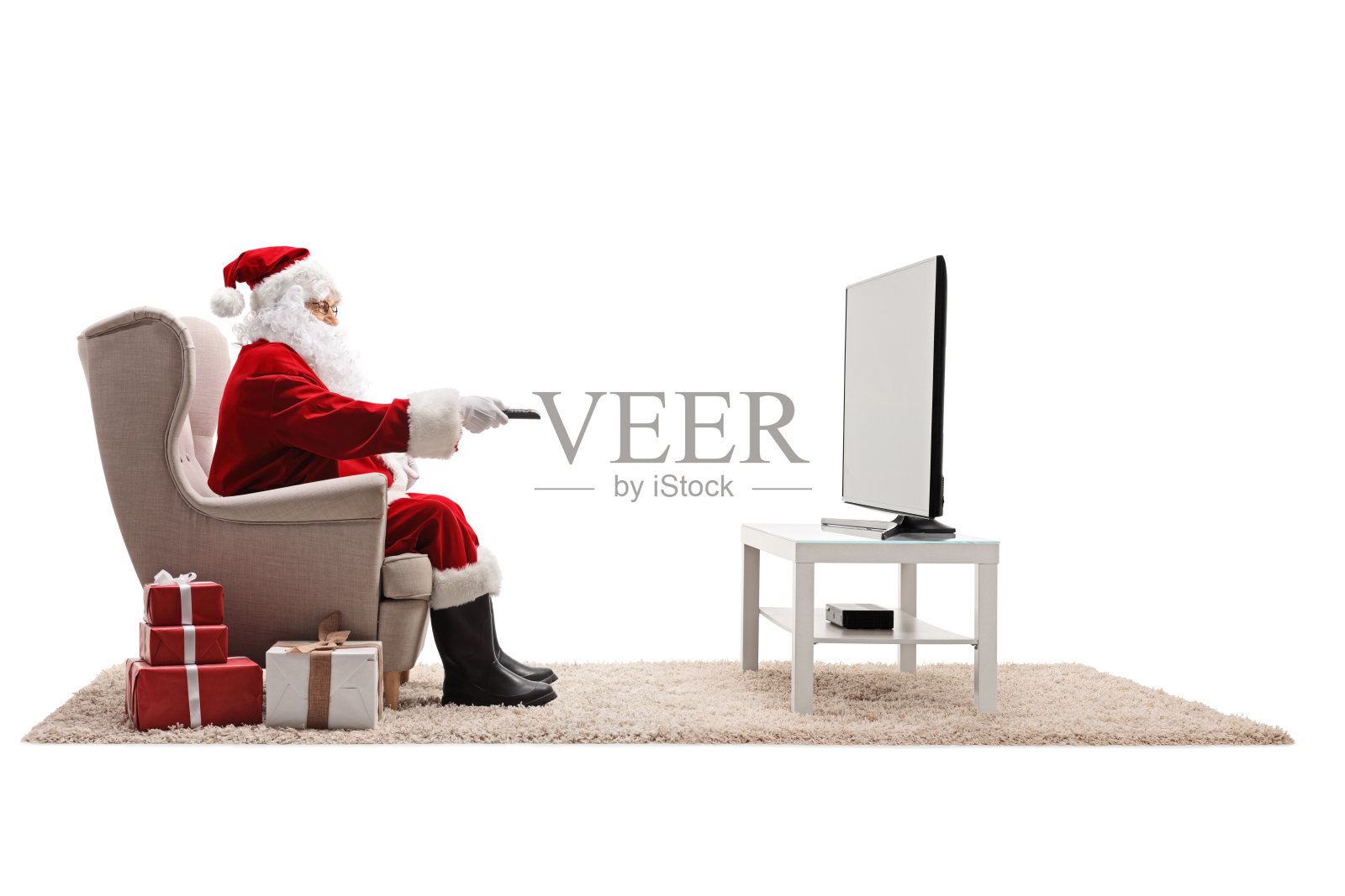 圣诞老人坐在扶手椅上，用遥控器看电视照片摄影图片