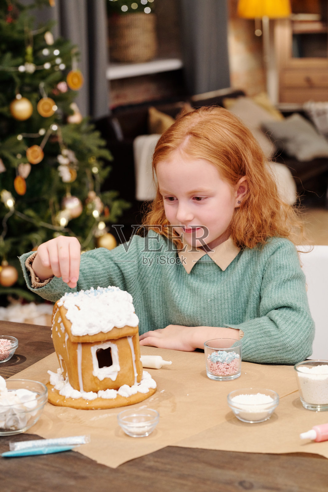 可爱的女孩洒水的姜饼屋屋顶装饰着鲜奶油照片摄影图片