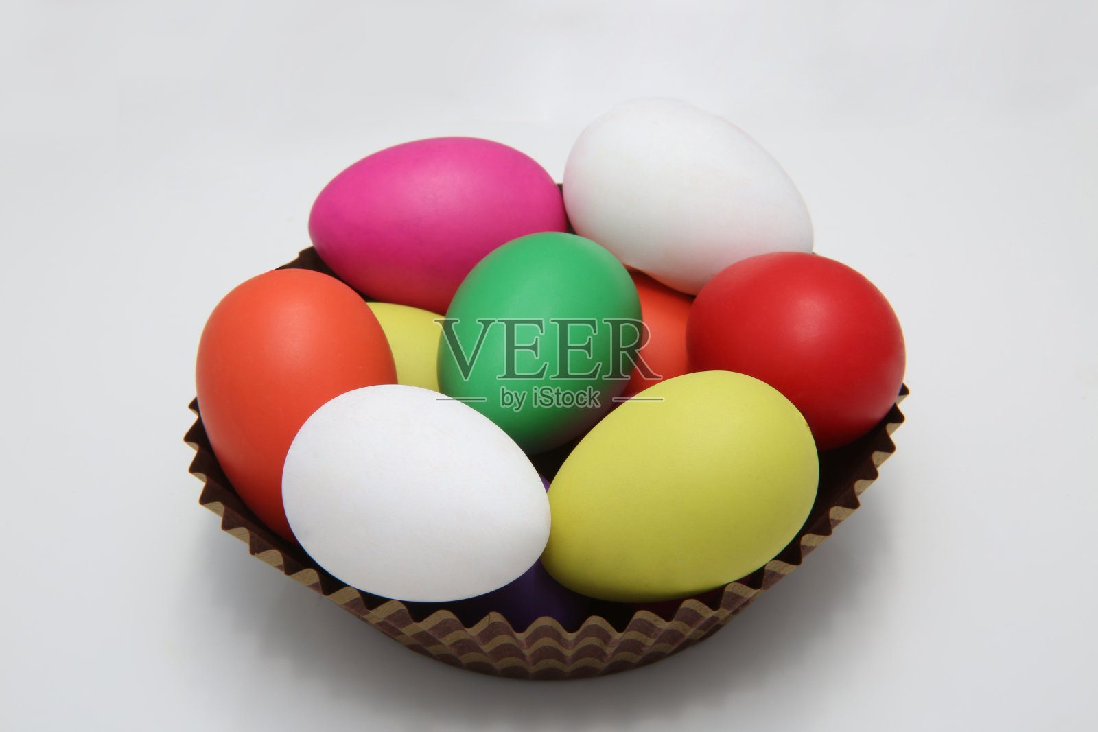 五彩缤纷的复活节彩蛋，红，粉，黄，绿，白，在一个棕色的纸篓里，以白色为背景。照片摄影图片