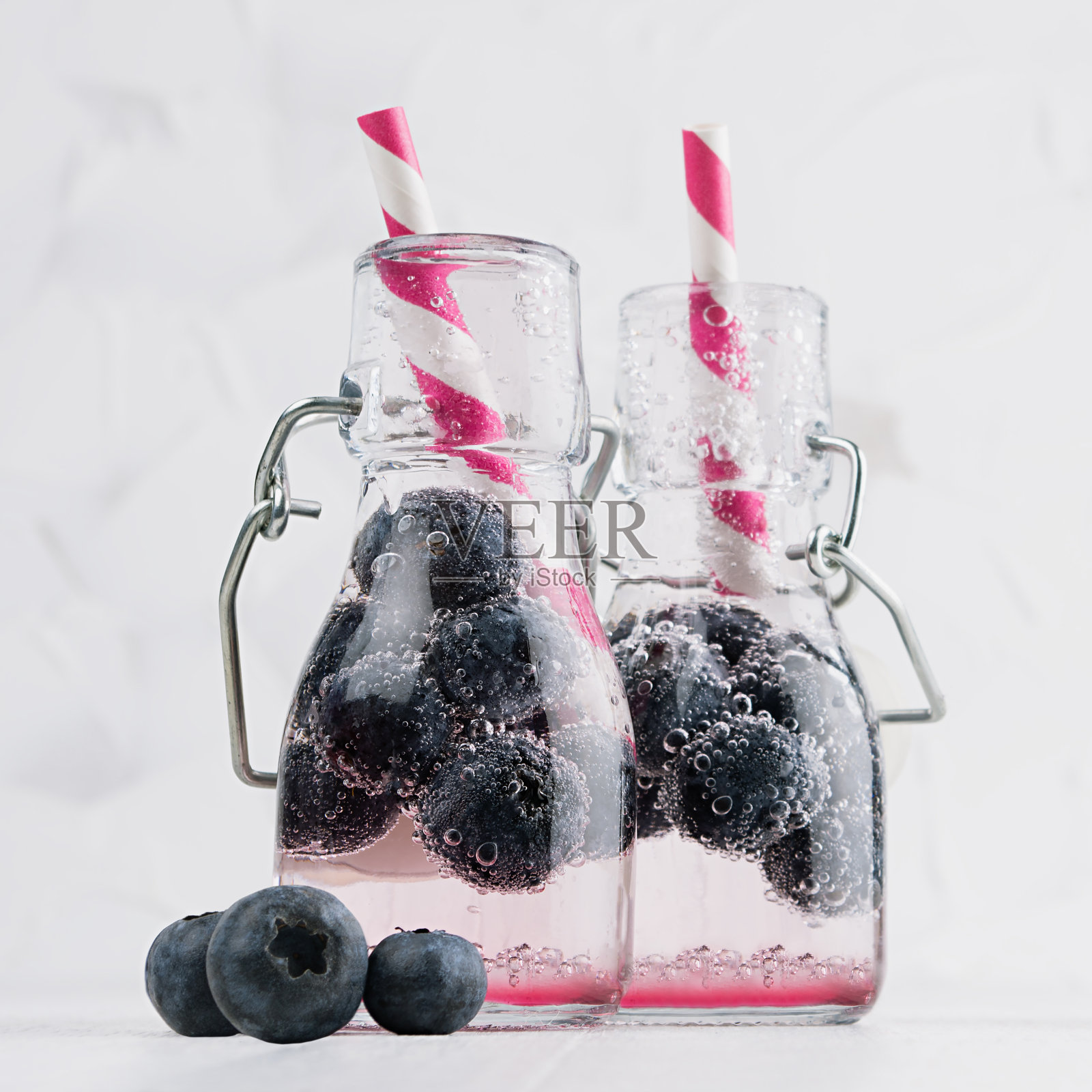 欢乐清新的夏季饮料与蓝莓，稻草，苏打水优雅的轭架瓶在柔和的轻白色木桌，方形。照片摄影图片