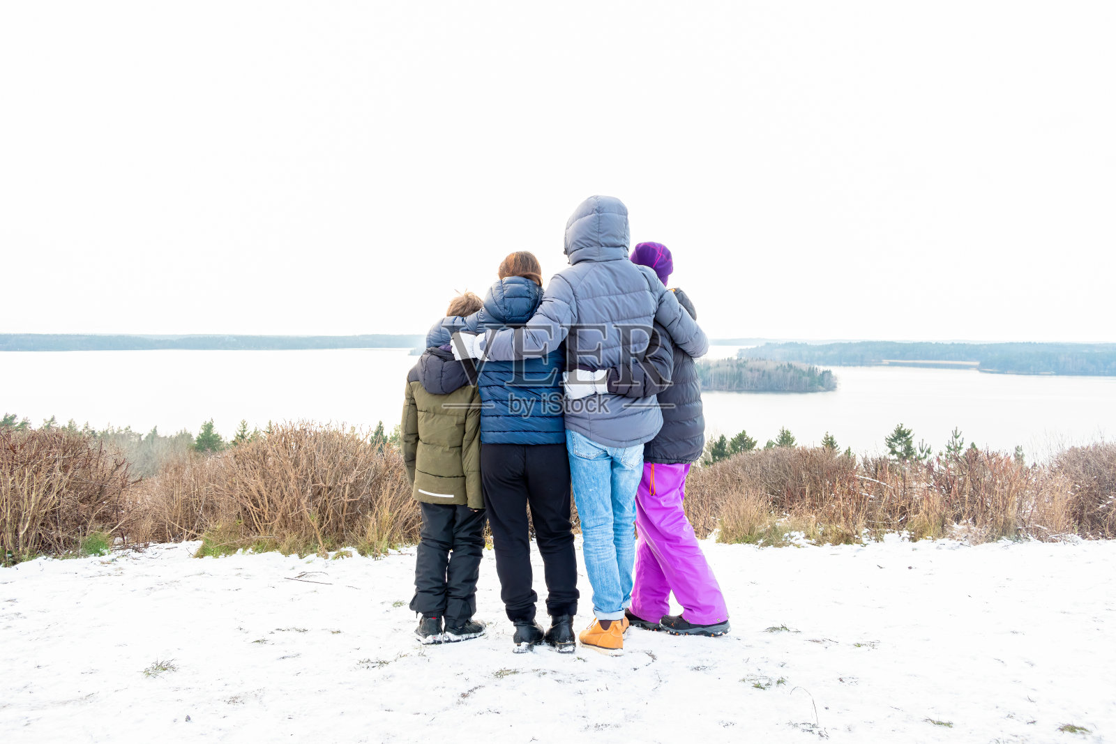 家人在一起互相抱着看风景。山顶上的冬季雪景有水和地平线。照片摄影图片