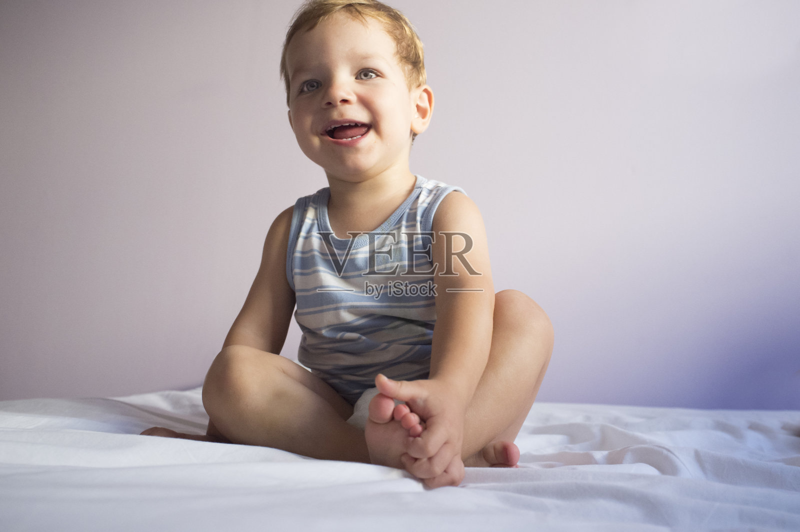 很开心的2岁男孩坐在床上照片摄影图片