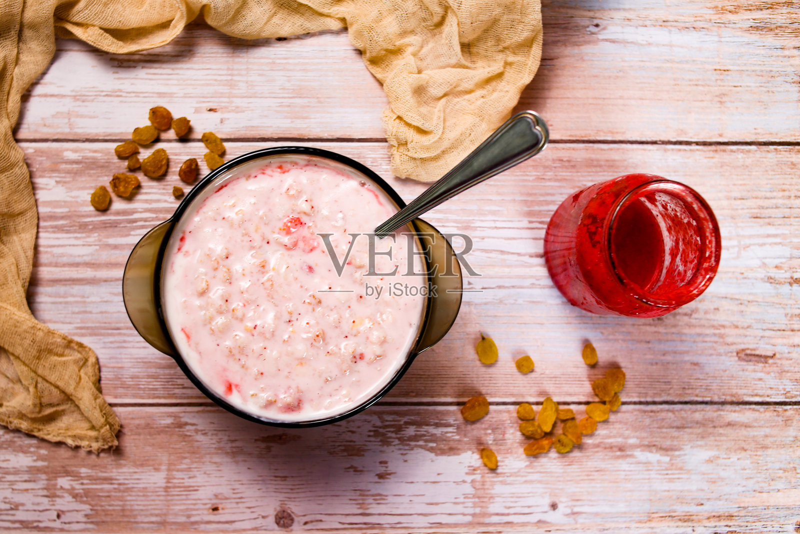 木桌上放着一杯加草莓、葡萄干和草莓酱的燕麦粥。为孩子在家提供美味健康的食物。照片摄影图片