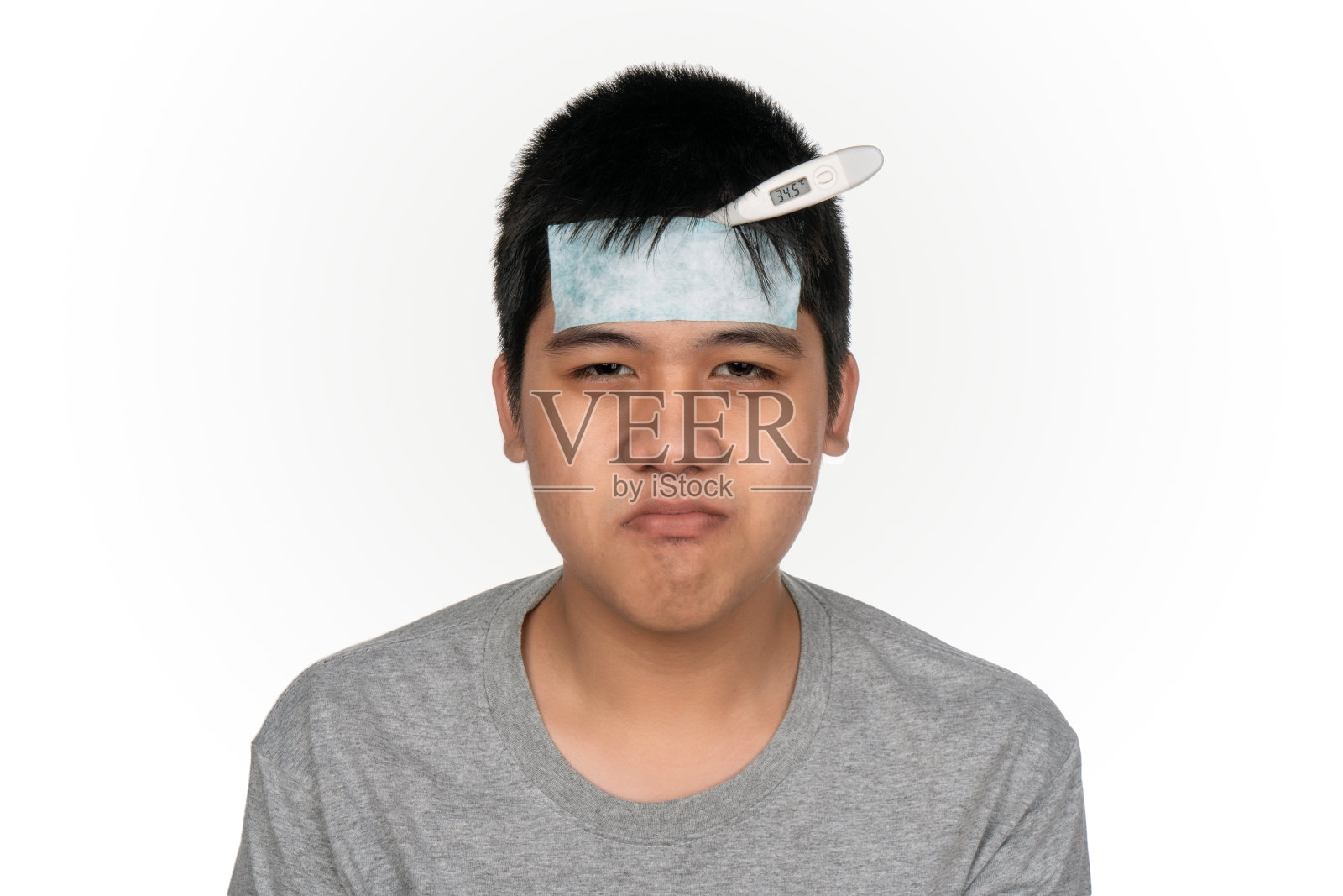 头部拍摄不愉快的近距离生病的亚洲男孩头痛与凉爽的包装和使用数字温度计在错误的方式孤立在白色背景。照片摄影图片