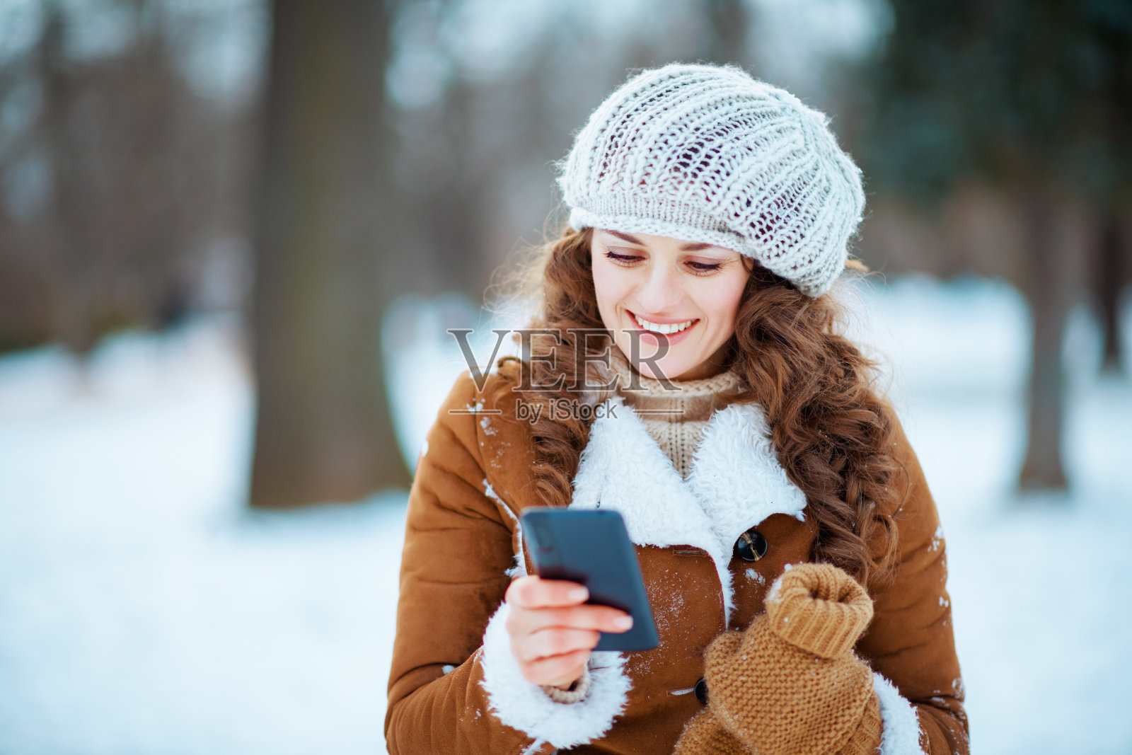 微笑的女人在冬天的城市公园里使用手机应用程序照片摄影图片