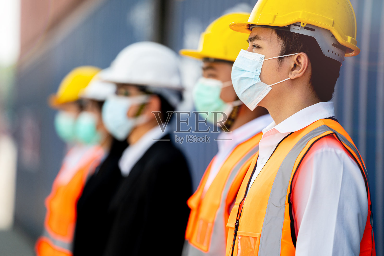 图为工人戴着防护面罩、安全帽和穿着工作服、安全服，背景是货仓。产业工人操作。人们有一个社交距离空间。照片摄影图片