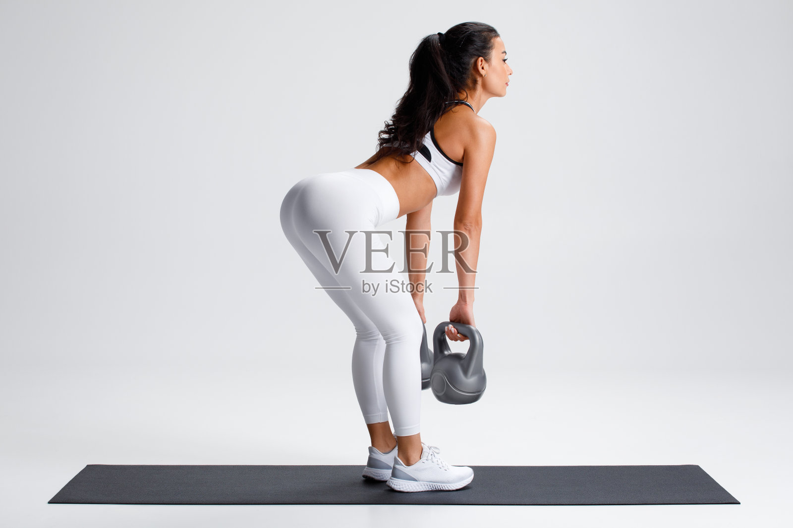 健身妇女做硬举运动的臀大肌在灰色的背景。运动女孩用壶铃锻炼照片摄影图片