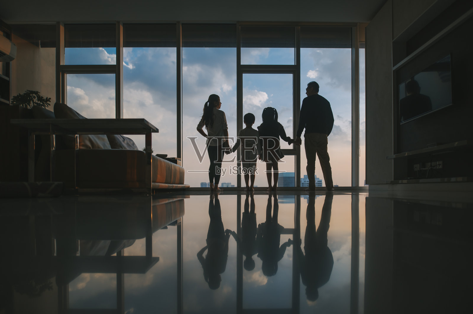 剪影后视图亚洲华人家庭和两个孩子看透过窗户欣赏美丽的日落在吉隆坡城市的客厅照片摄影图片