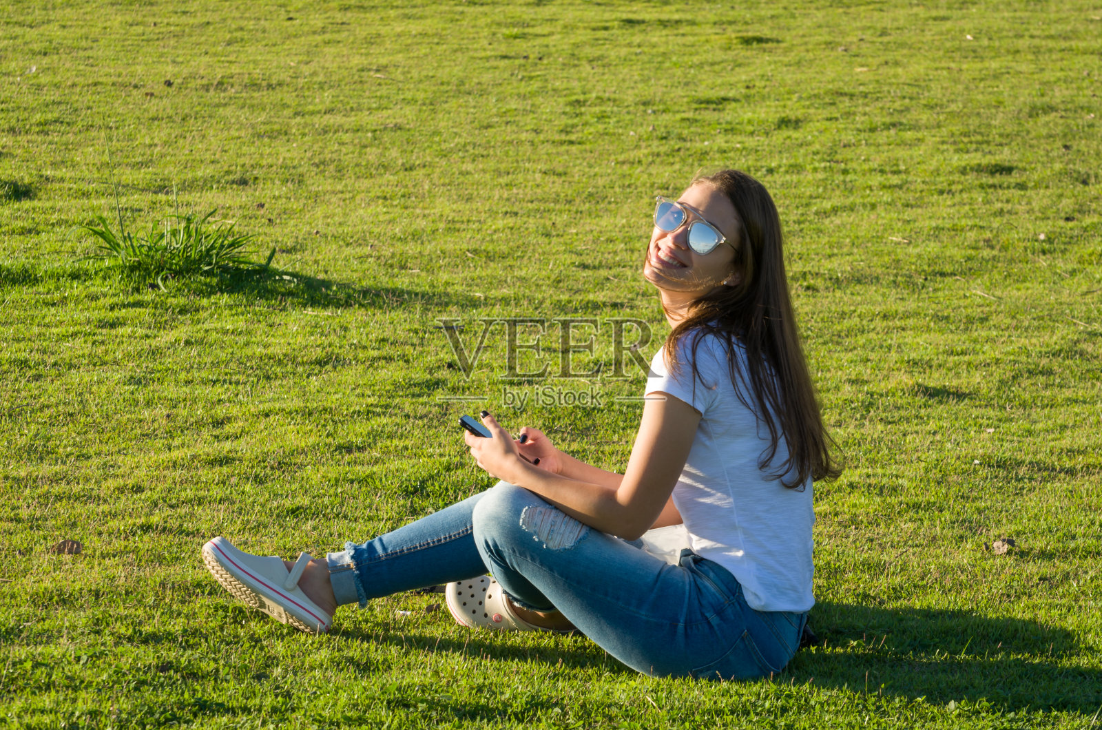 年轻女子坐在草地上，用智能手机在新奥拉做Guaiba上照片摄影图片