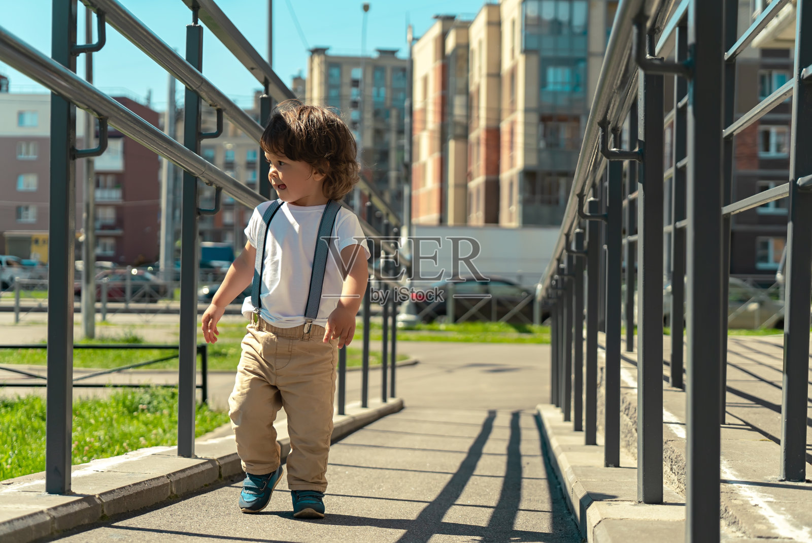 长发可爱的蹒跚学步的小男孩走在城市街道外面的斜坡上照片摄影图片