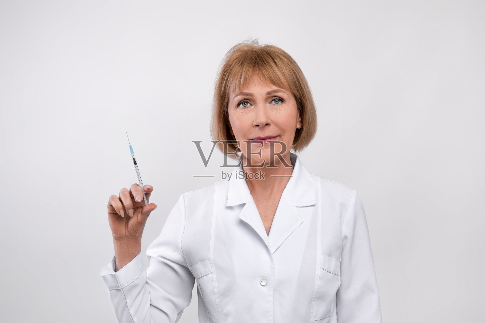 成年女医生身穿白大褂，手持装有药物、疫苗或美容注射剂的注射器照片摄影图片