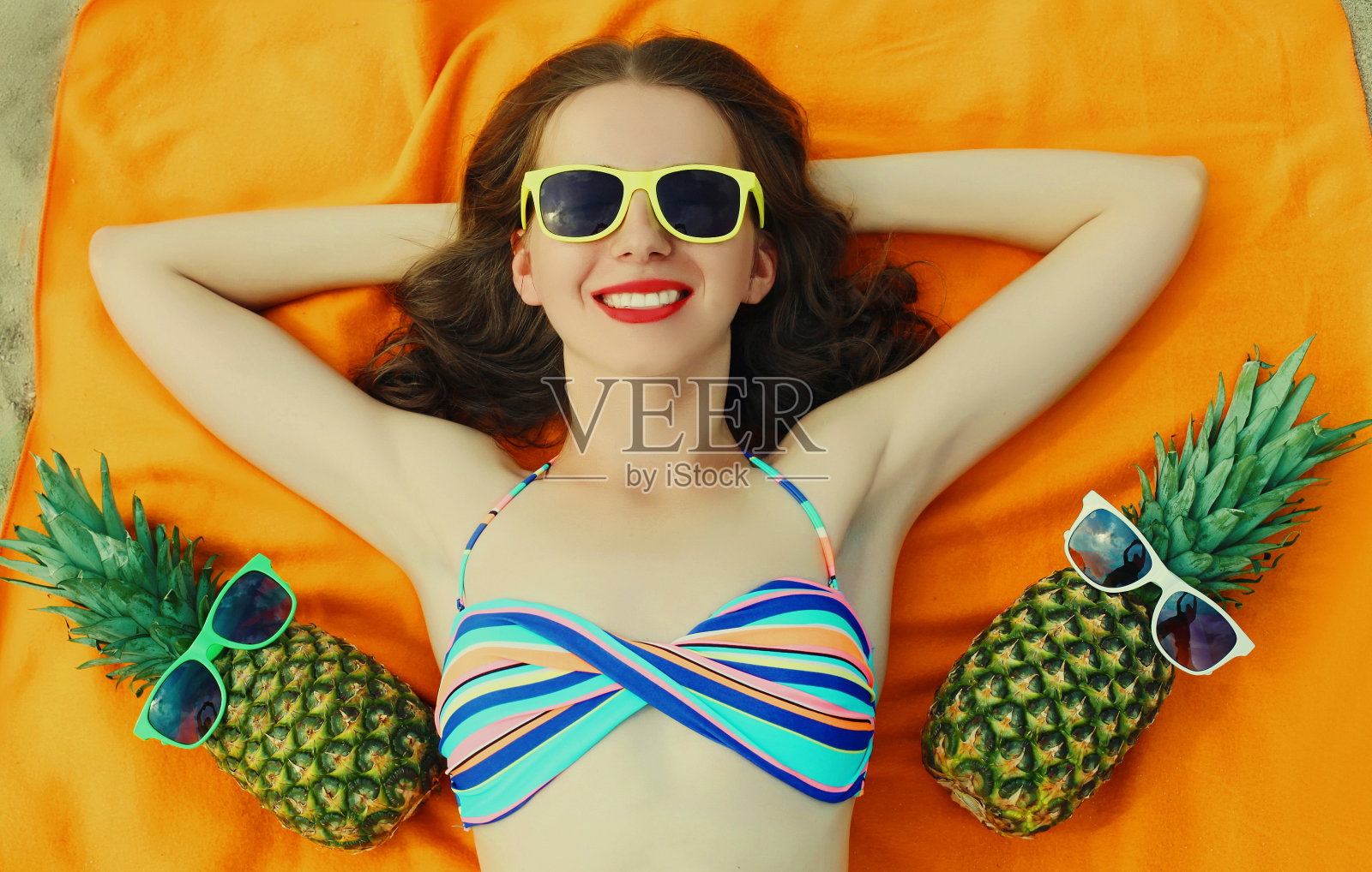 快乐微笑的年轻女子的肖像躺在一个有趣的菠萝戴着太阳镜的海滩上照片摄影图片