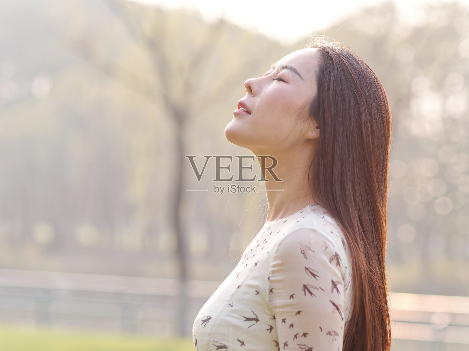 近距离拍摄的美丽的年轻中国女人，抬起头，在阳光下闭上眼睛照片摄影图片