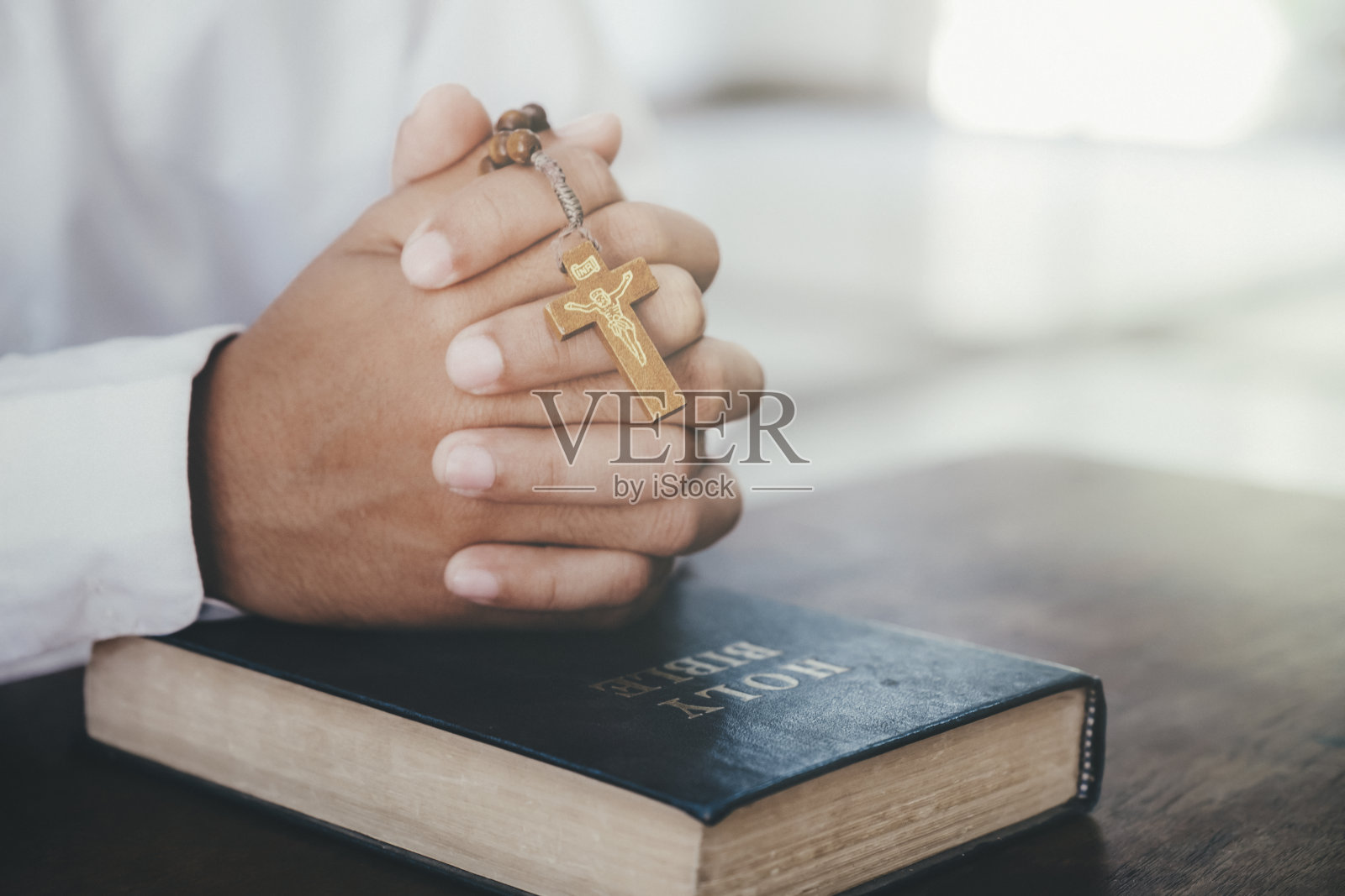 男人在祈祷，双手合十放在她的圣经上。照片摄影图片