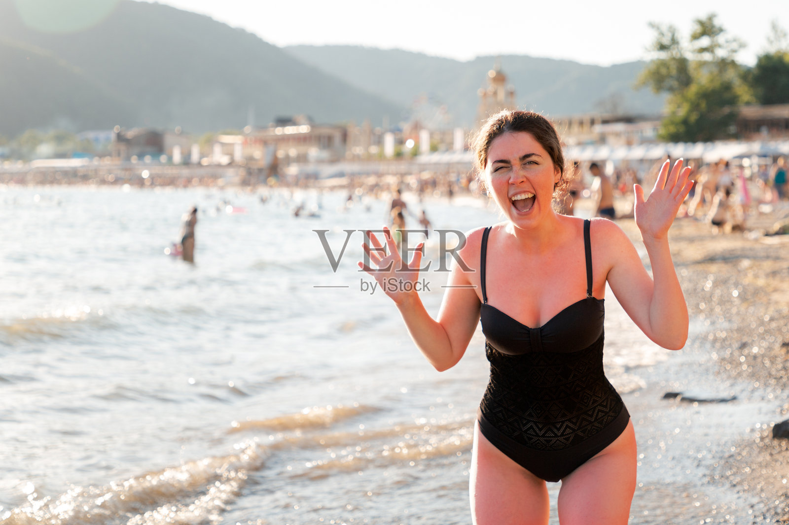 皮肤护理。一个年轻的女人在海上晒太阳时被晒伤后尖叫。红色的皮肤。背景是海滩和大海。使用防晒霜的概念照片摄影图片