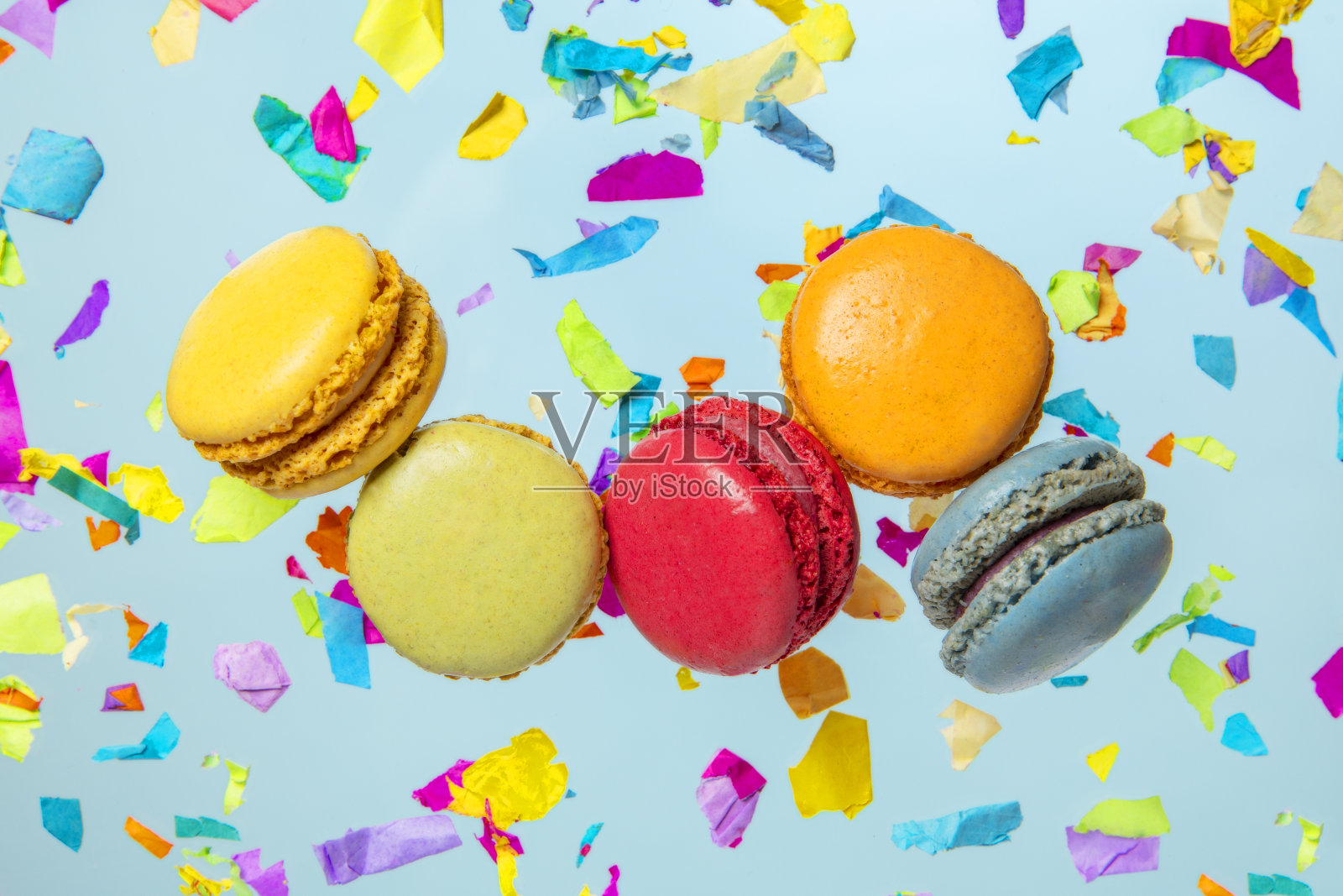 明亮的多色马卡龙饼干甜糕点在蓝色的派对五彩纸屑背景照片摄影图片