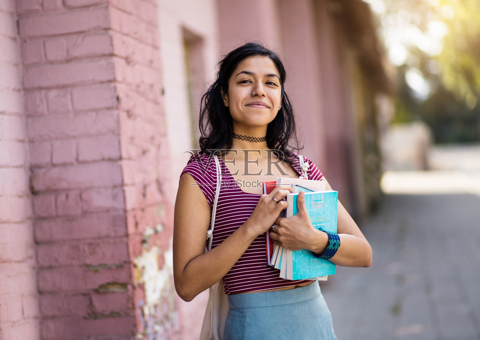 年轻的女学生站在街上拿着书。照片摄影图片