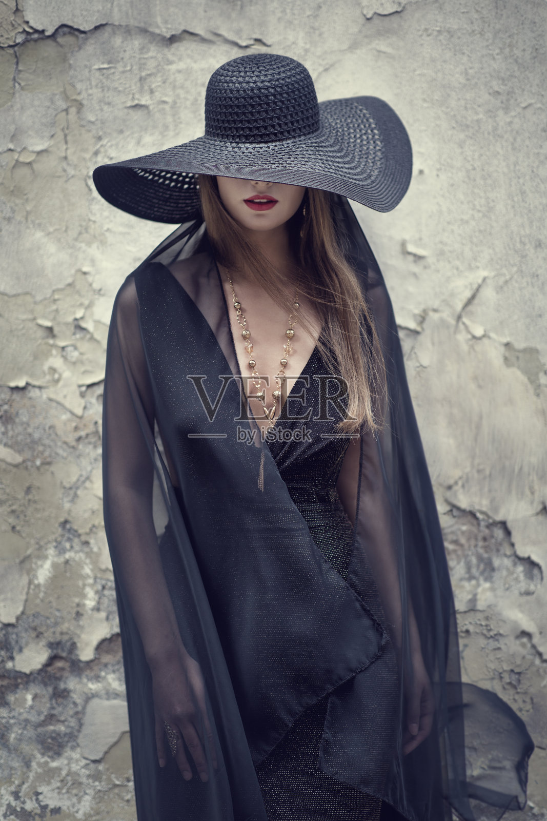 高级时装模特在黑帽隐藏脸Grunge墙背景。时尚女性肖像与红唇和项链珠宝。优雅复古的女士照片摄影图片