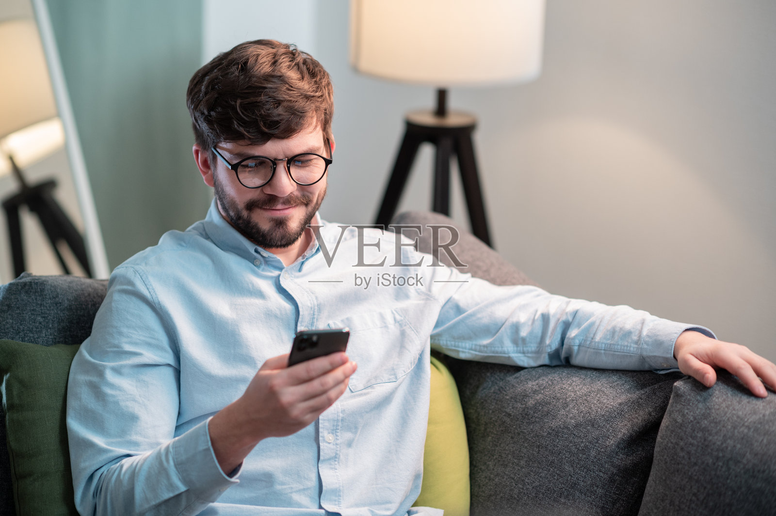 一个可爱的男孩坐在家里的沙发上，手里拿着手机，和朋友聊天发短信照片摄影图片