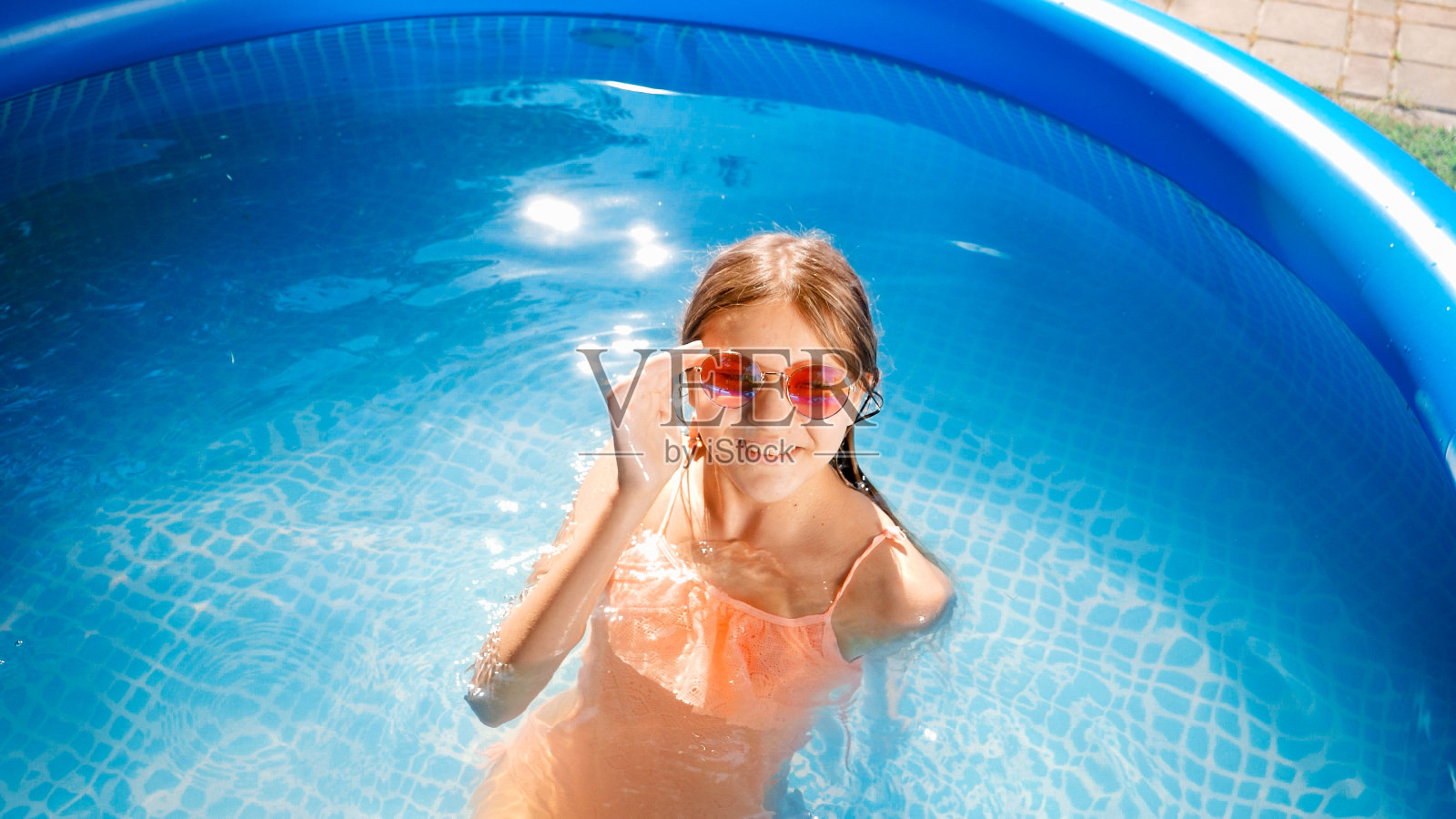 美丽微笑的女孩戴着太阳镜在游泳池里游泳和放松，看着镜头照片摄影图片