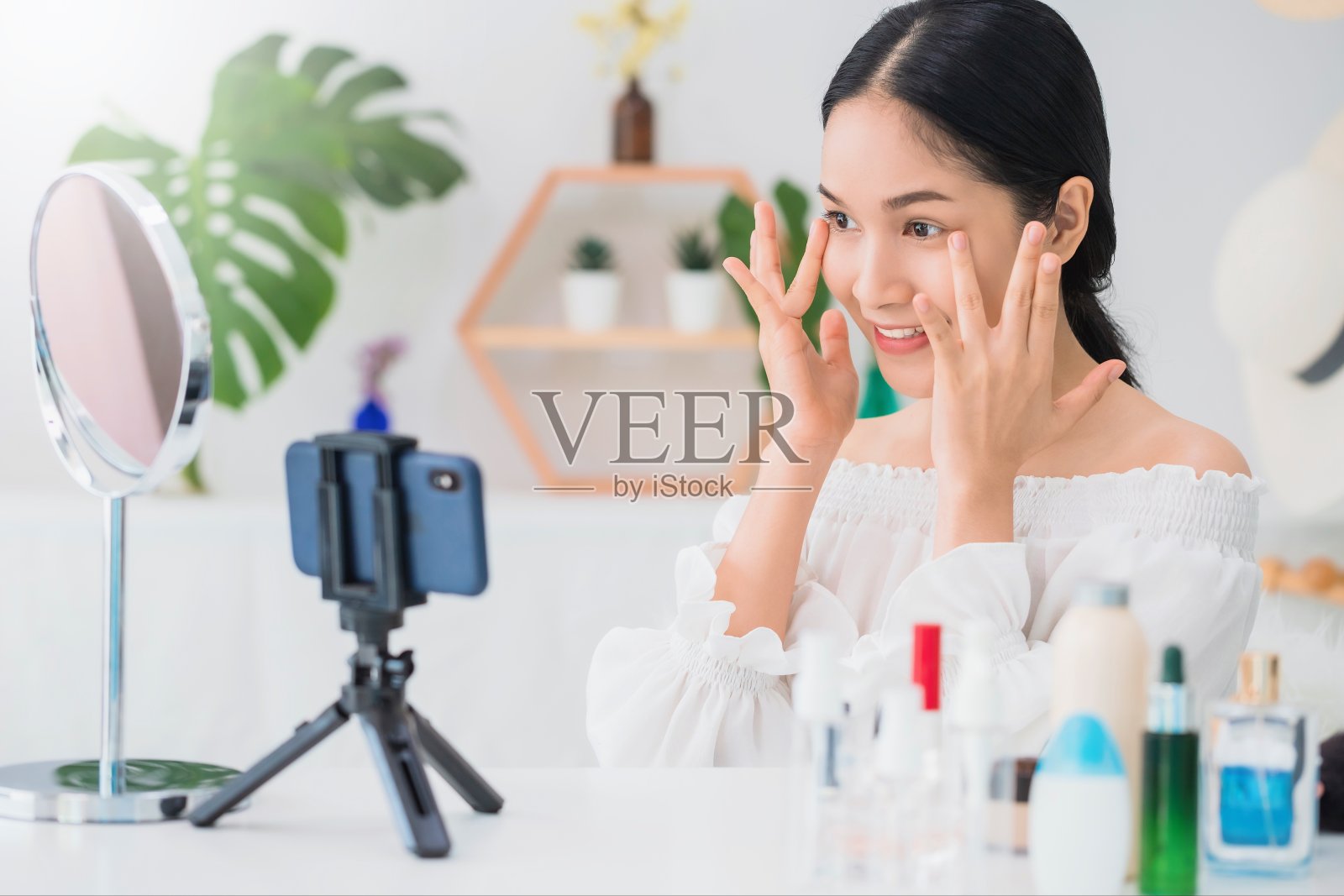 美丽的亚洲女人博客展示如何化妆和使用化妆品。在家用镜子和智能手机录制视频直播。健康面部的护肤理念。照片摄影图片
