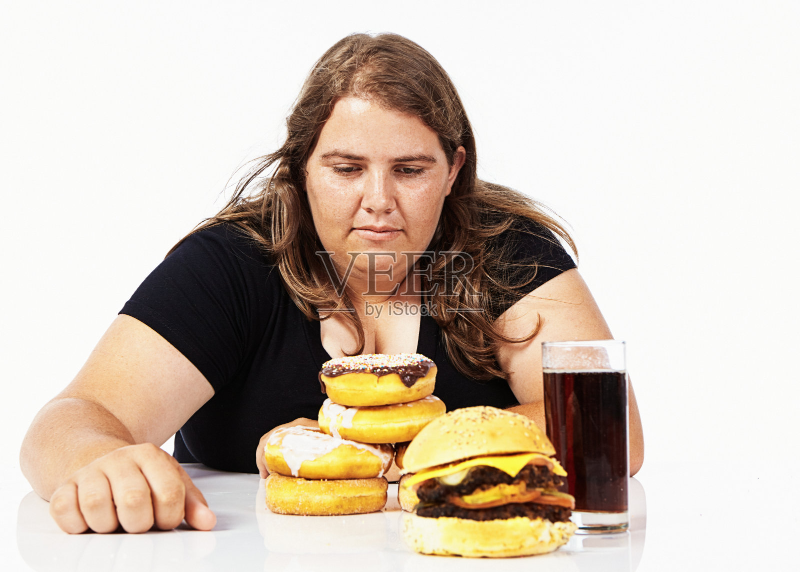 年轻女子坐在那里，面前放着甜甜圈、可乐和汉堡，看起来闷闷不乐照片摄影图片