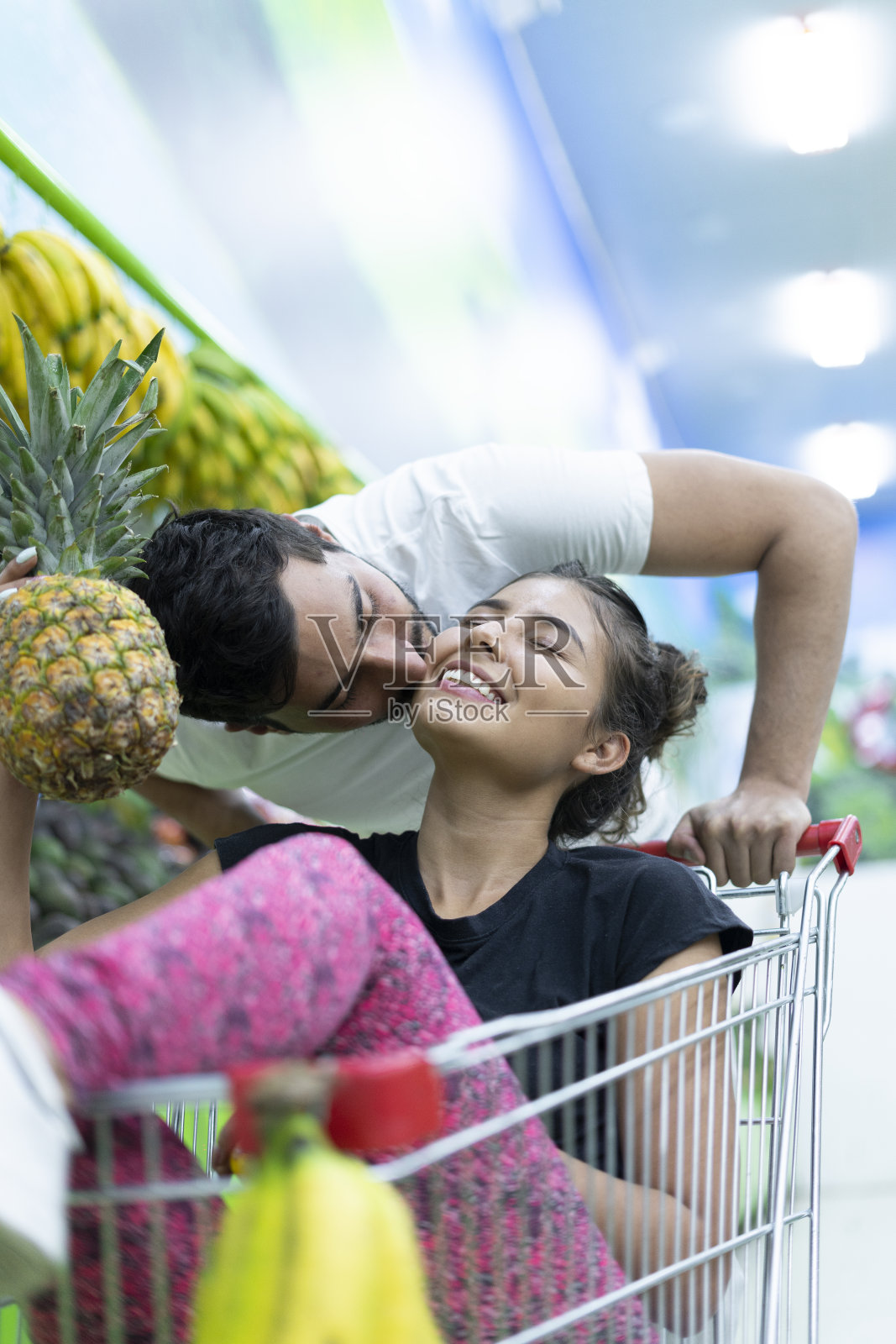 一对拉丁夫妇在杂货店里购物，妻子走进购物车，她的伴侣亲吻她照片摄影图片