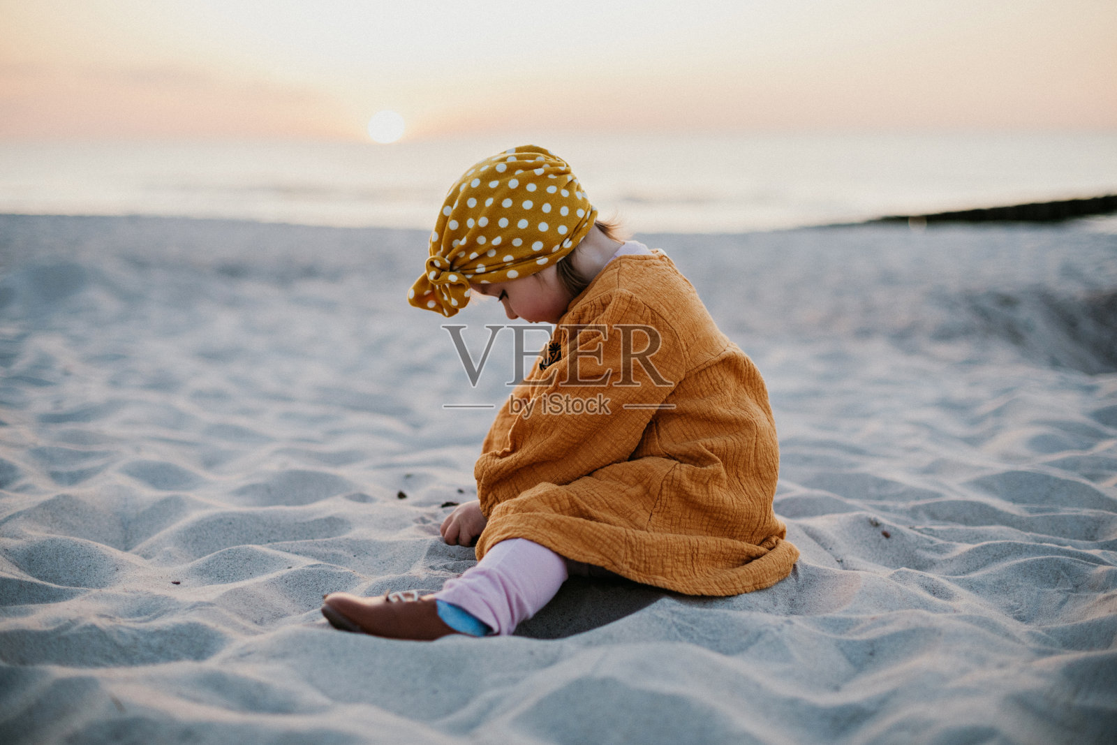 穿着东方服装的有趣的孩子坐在沙滩上玩沙子照片摄影图片