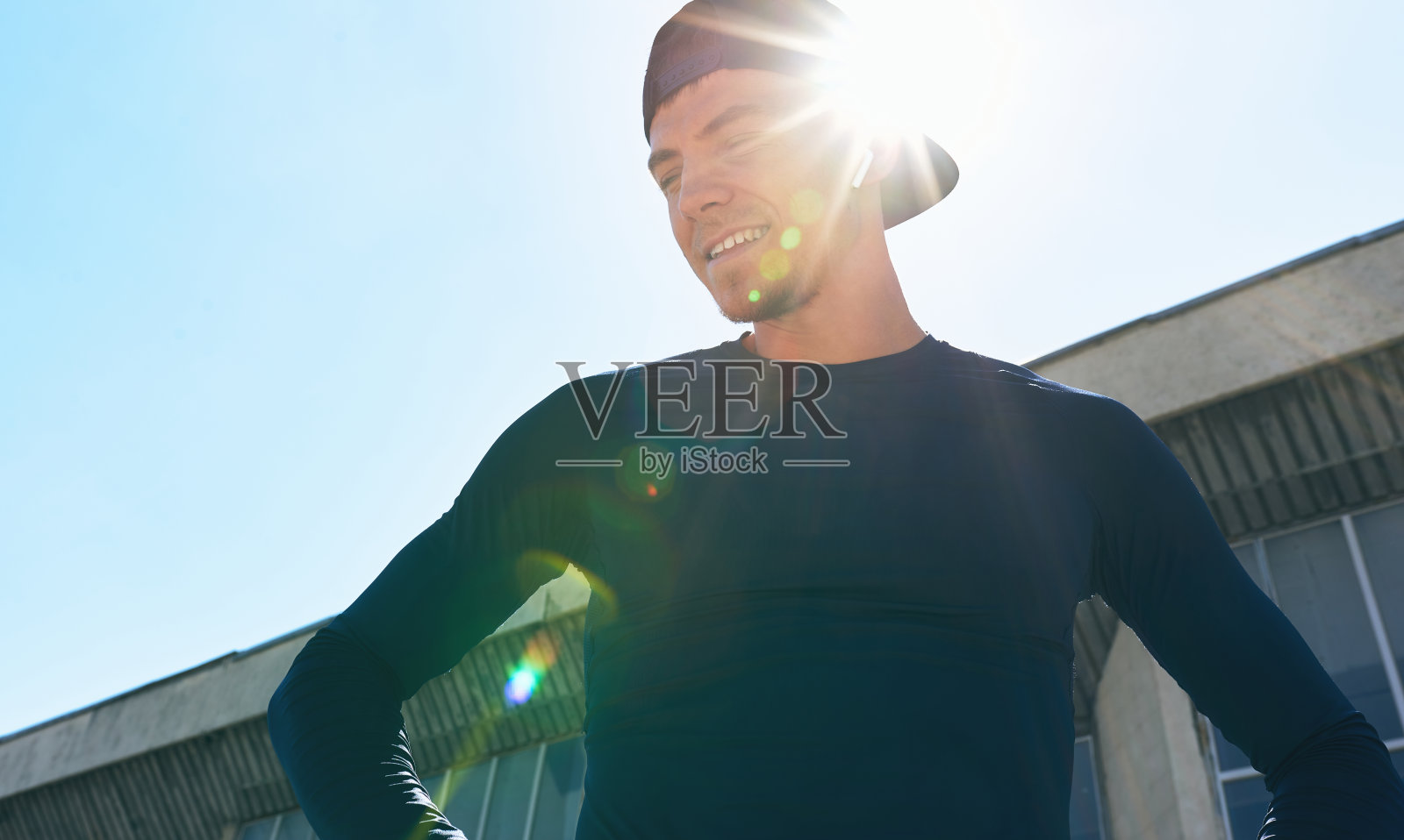一名运动员穿着运动服，双手放在腰部，在阳光下摆姿势。一个运动员在公园锻炼后休息的肖像。照片摄影图片