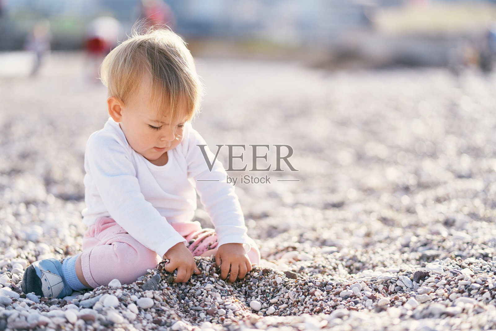 可爱的宝宝坐在卵石滩上挖洞照片摄影图片