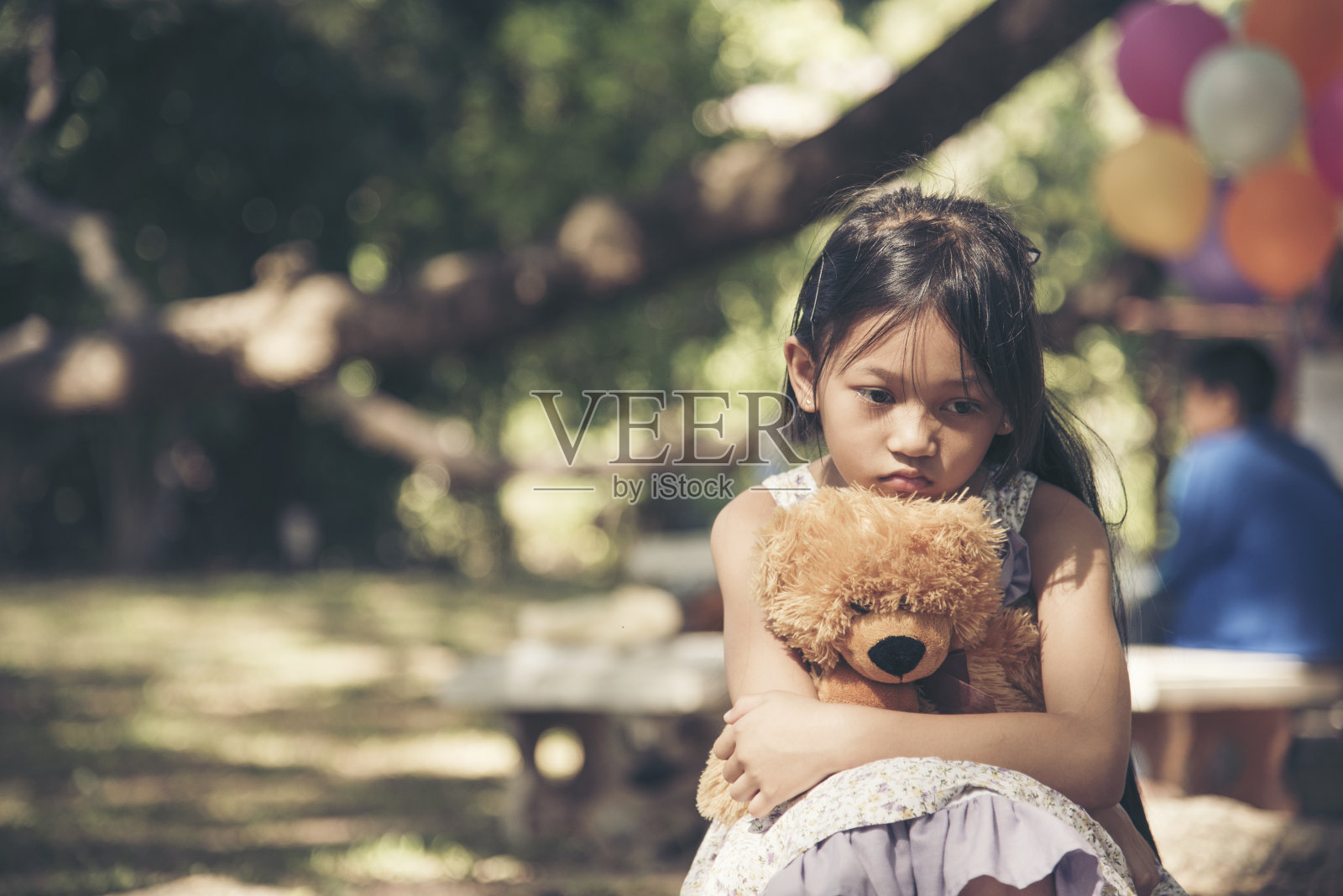 悲伤的女孩拥抱泰迪熊悲伤独自在绿色花园公园。孤独的女孩感觉伤心不快乐坐在户外与最好的朋友玩具。自闭症儿童玩泰迪熊最好的朋友。家庭暴力的概念照片摄影图片