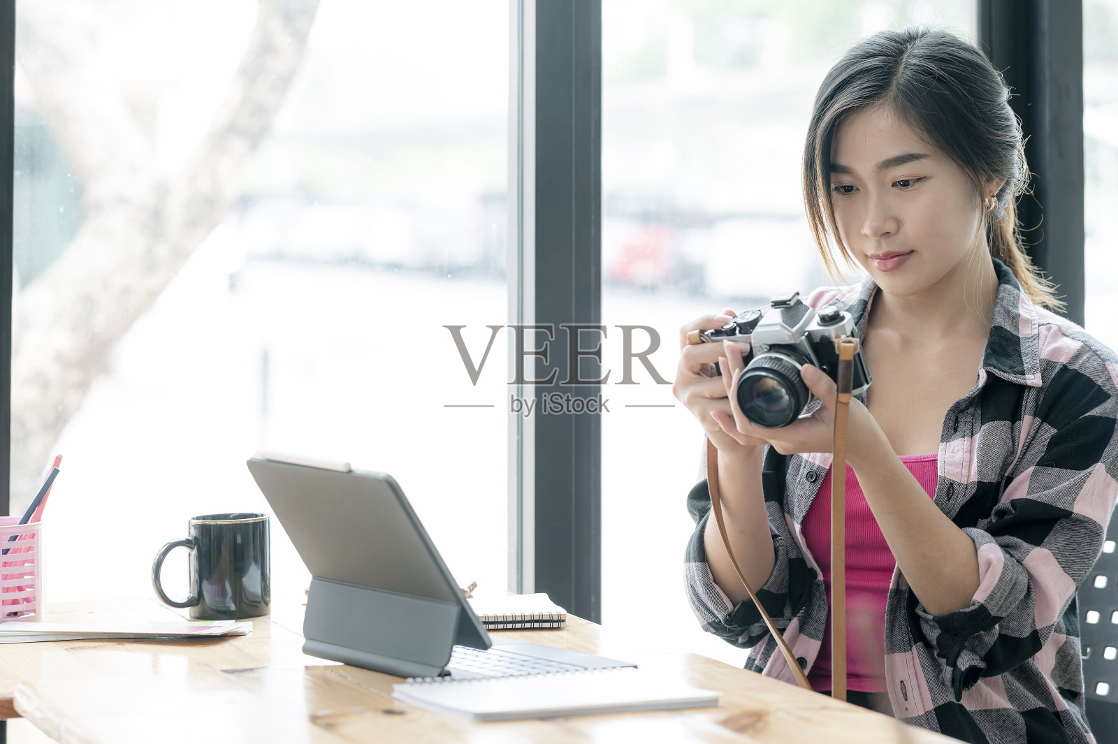 年轻美丽的亚洲摄影师拿着和看着相机屏幕，而坐在她的工作室。照片摄影图片