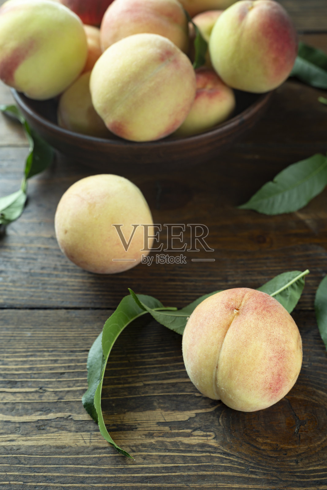 陶土碗里放着新鲜的桃子，放在质朴的木桌上。桃叶存在于成分中。照片摄影图片
