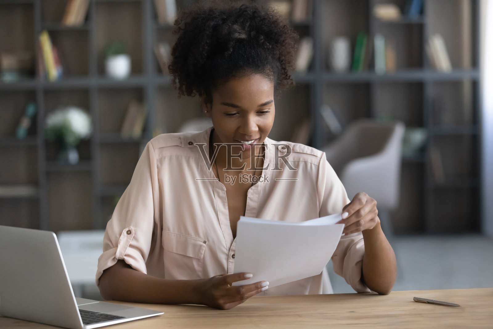 一位微笑的非裔美国妇女坐在办公桌前处理文件照片摄影图片