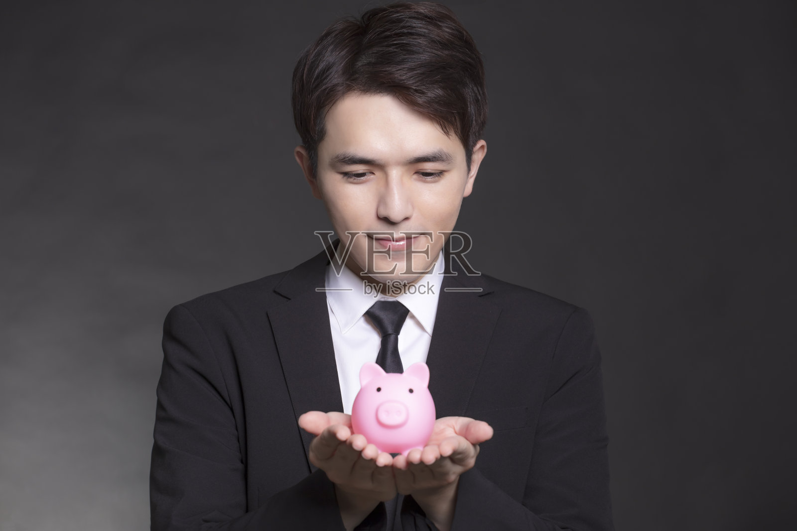 商人穿着黑色西装，手里拿着粉红色的存钱罐照片摄影图片