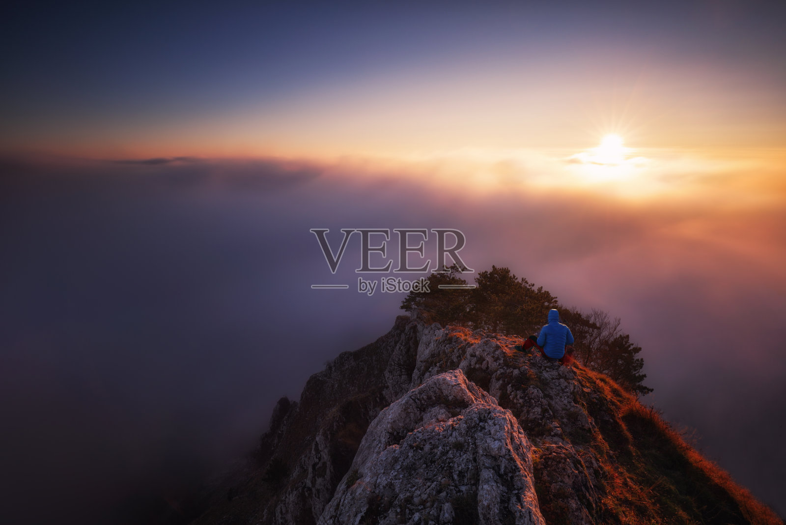 戏剧性剪影的人坐在山脊上俯瞰雾蒙蒙的天空照片摄影图片