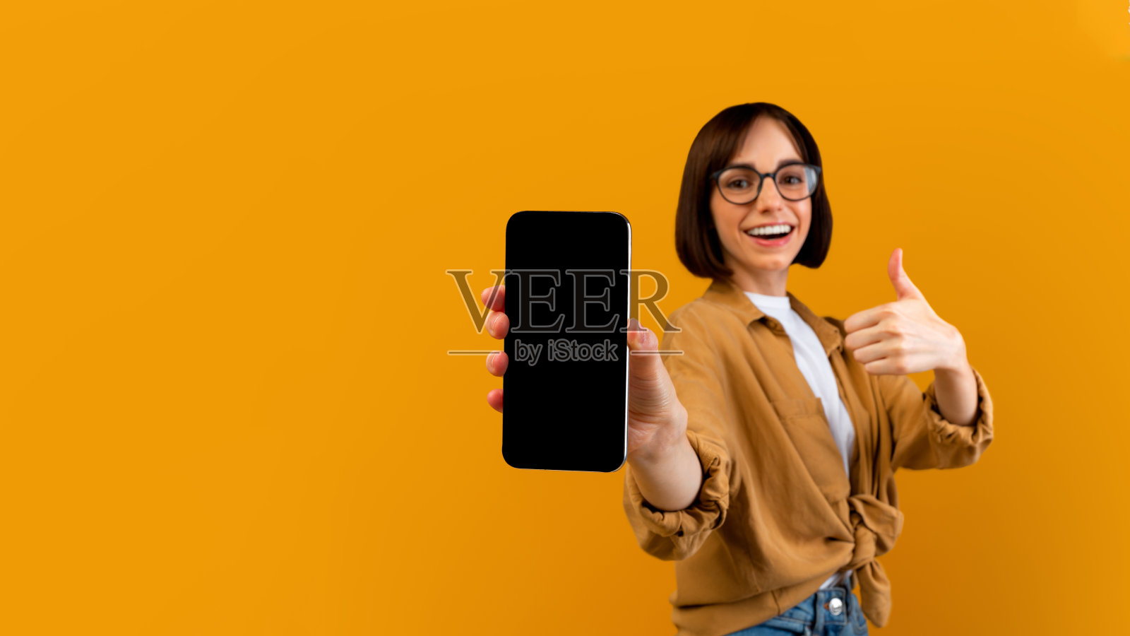 兴奋的女士拿着黑屏智能手机，竖起大拇指，推荐新的应用程序或网站照片摄影图片