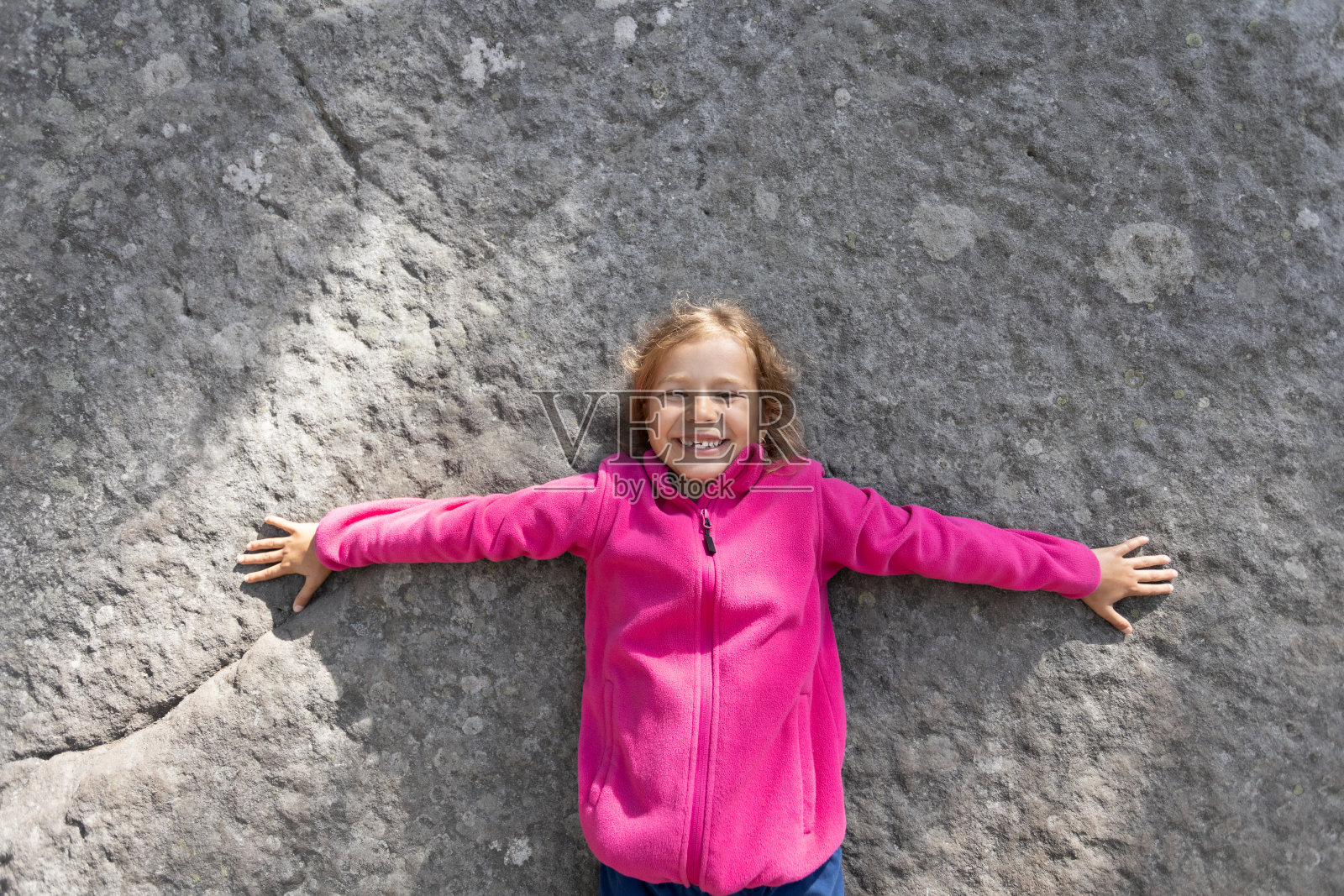 可爱的金发小女孩在大岩石背景下微笑。照片摄影图片