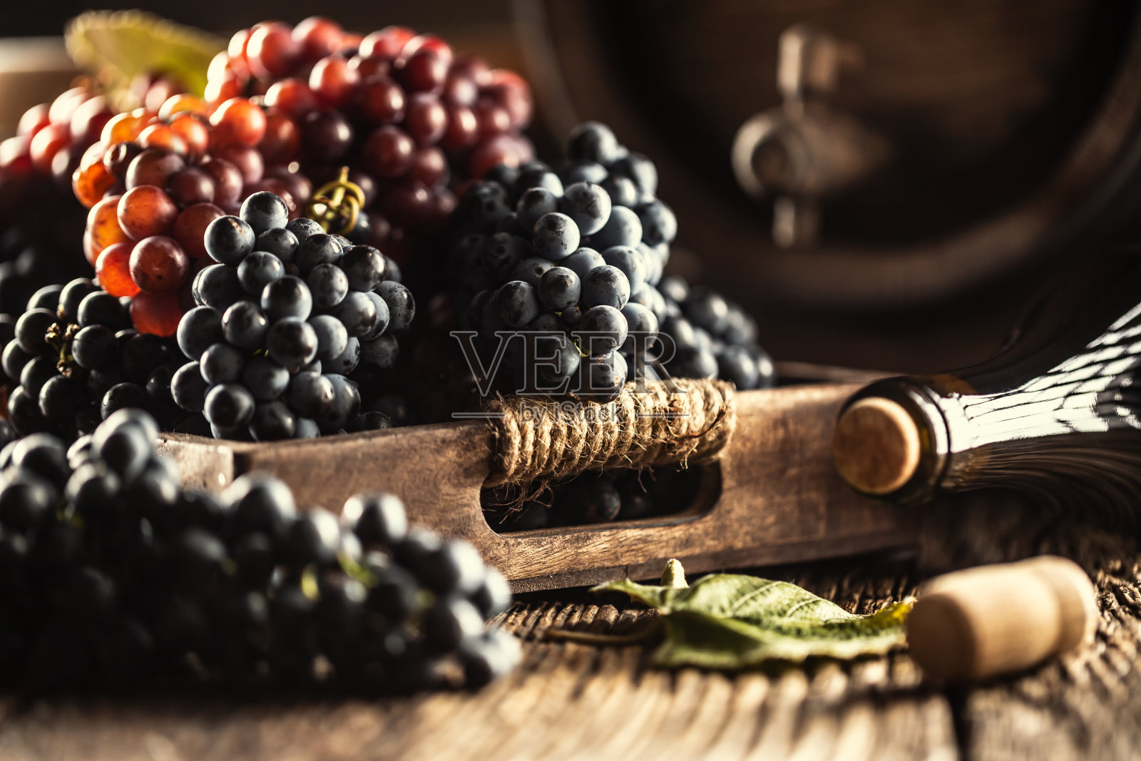 只是把成熟的葡萄松散地放在一个木盒子里，背景是一个酒桶和一瓶红酒。照片摄影图片
