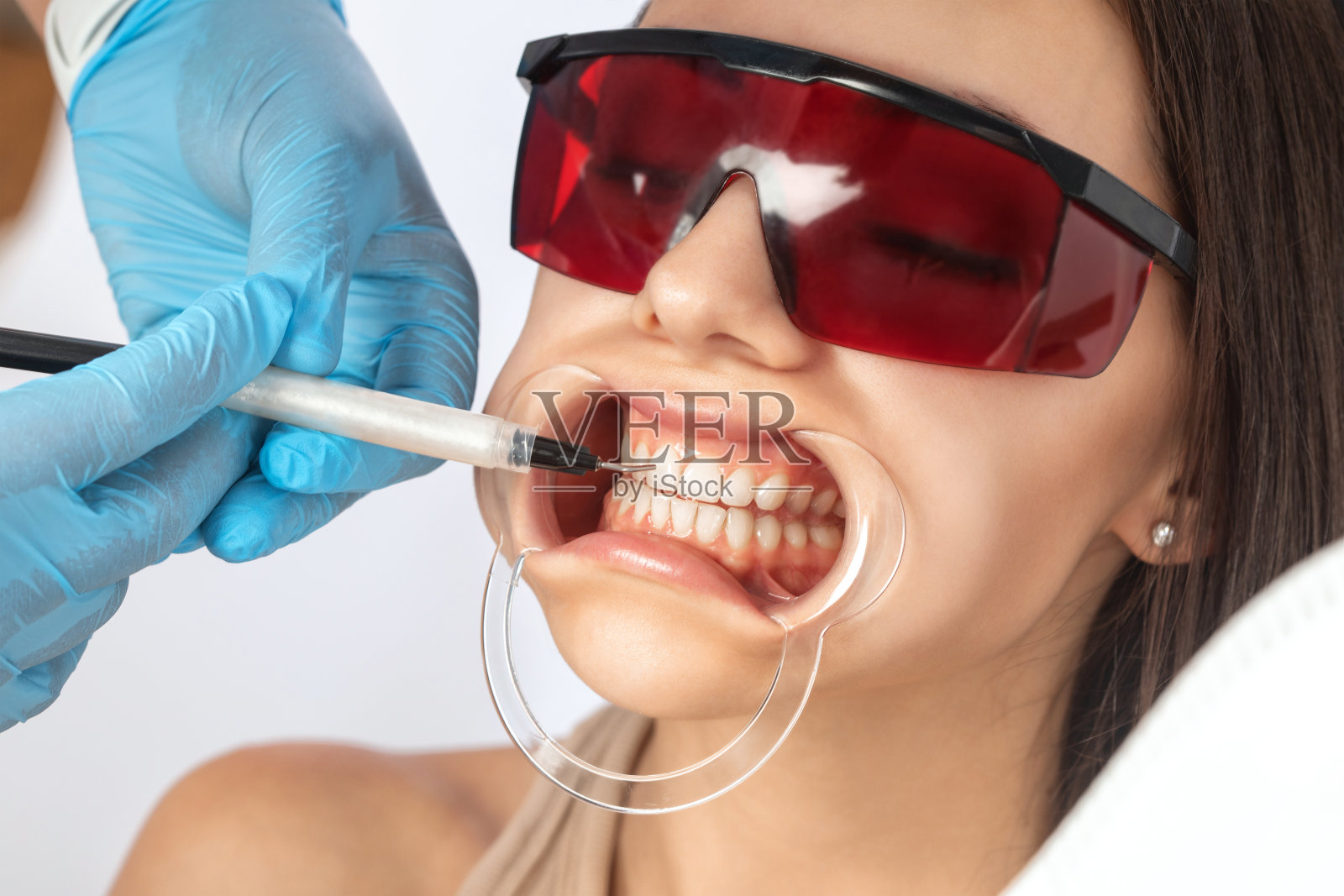 牙医在诊所给一位年轻漂亮的女士做牙齿美白手术。一个健康的微笑。照片摄影图片