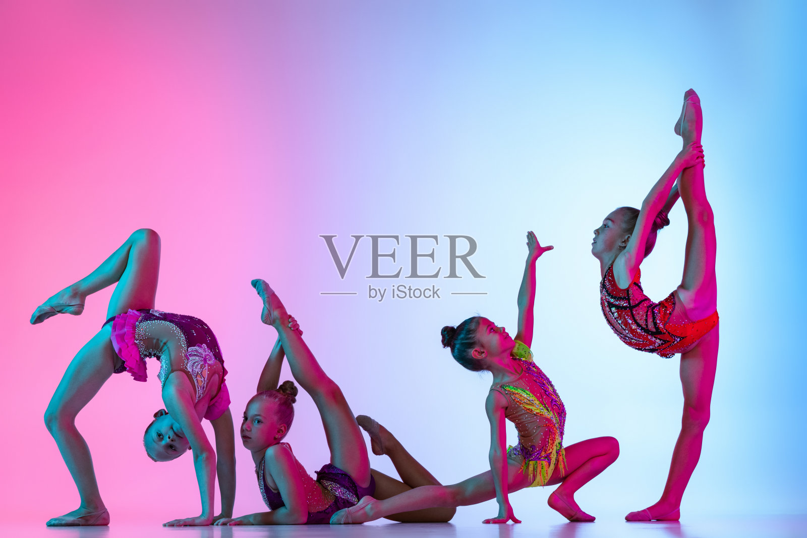 一群美丽灵活的艺术体操艺术家，女孩在体育事件孤立在梯度粉红色的蓝色工作室背景在霓虹灯照片摄影图片